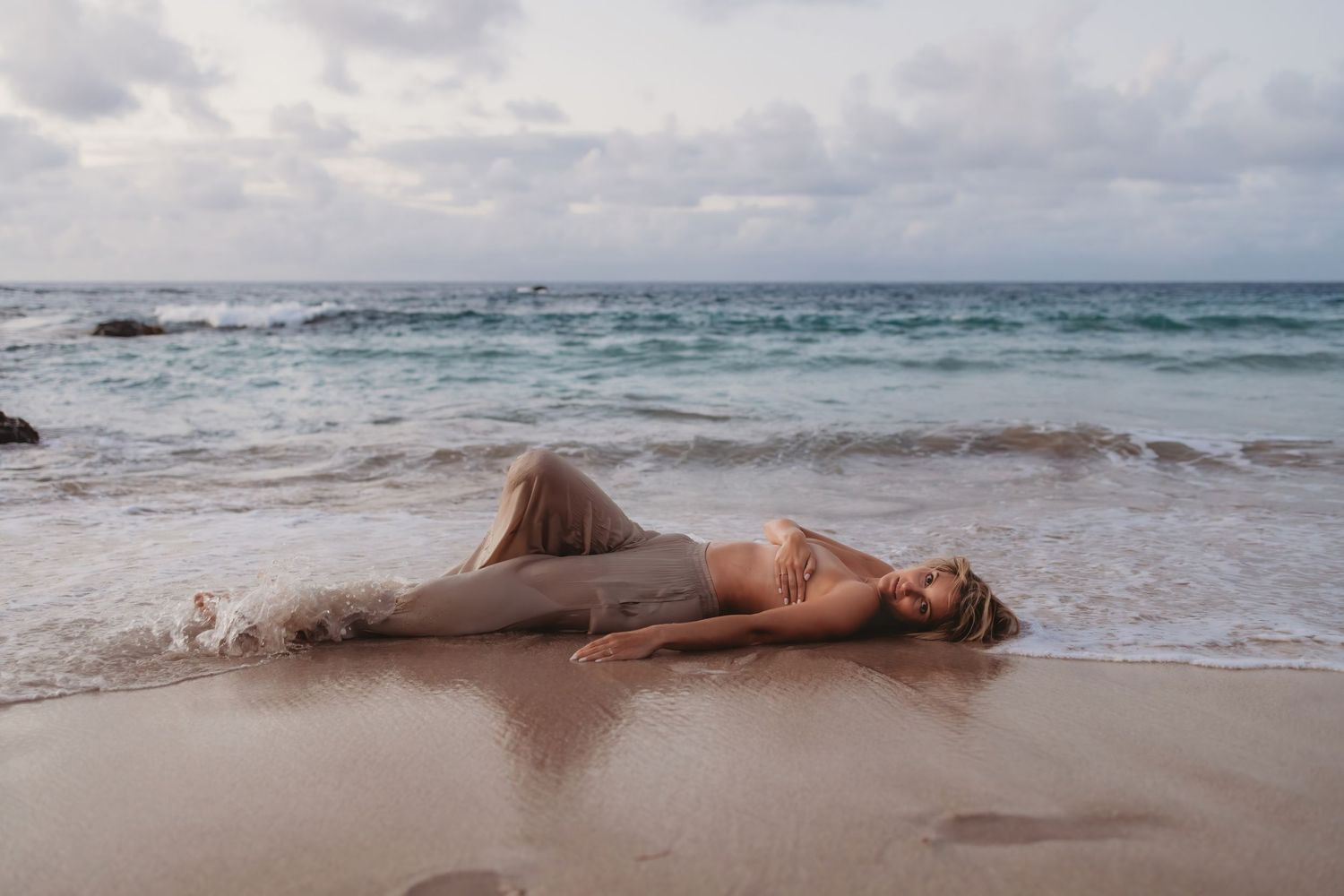 Artful branding photo of a woman laying in the shoreline surf.