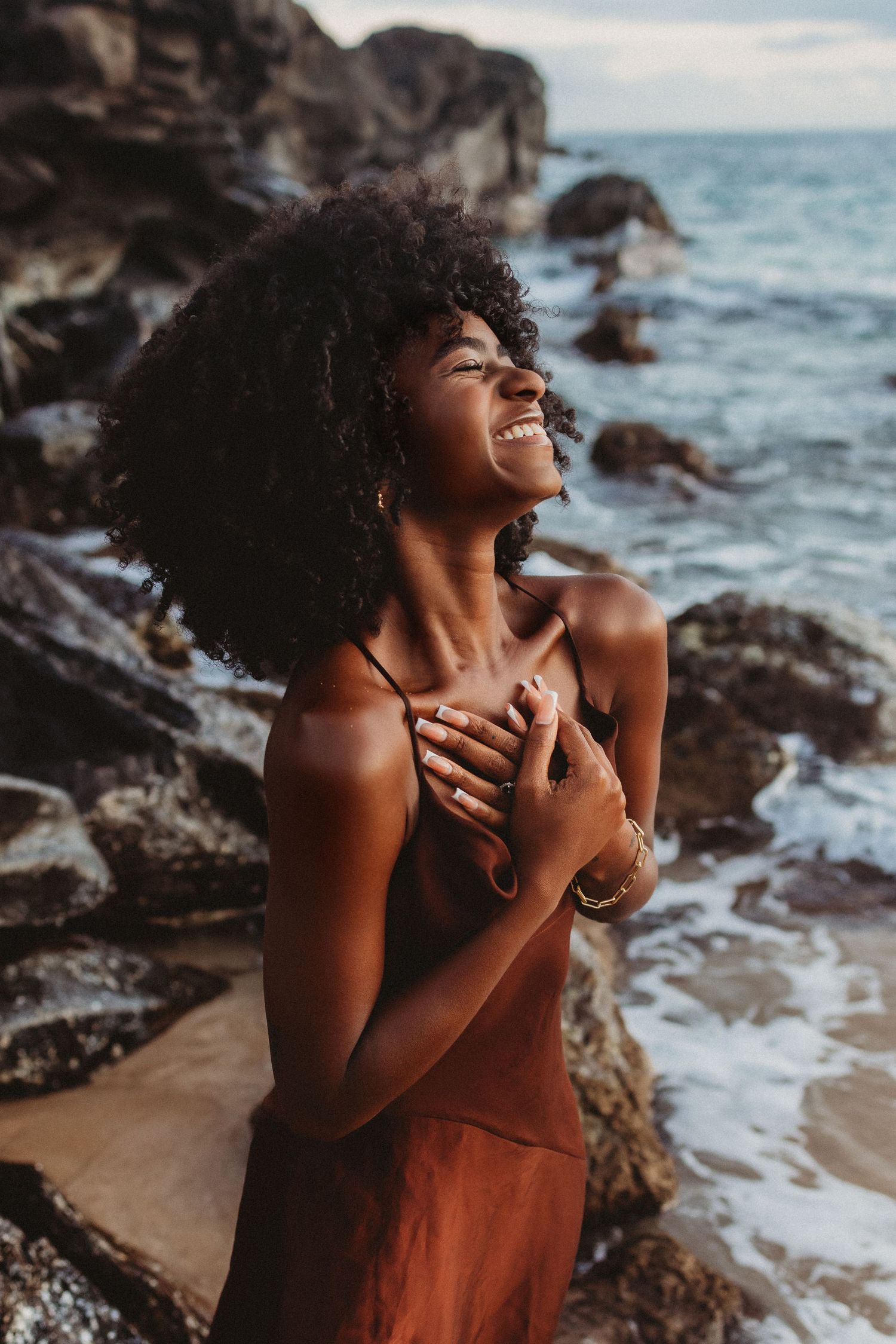 Maui Lifestyle brand image featuring a laughing woman posed on coastal rocks in the sea.