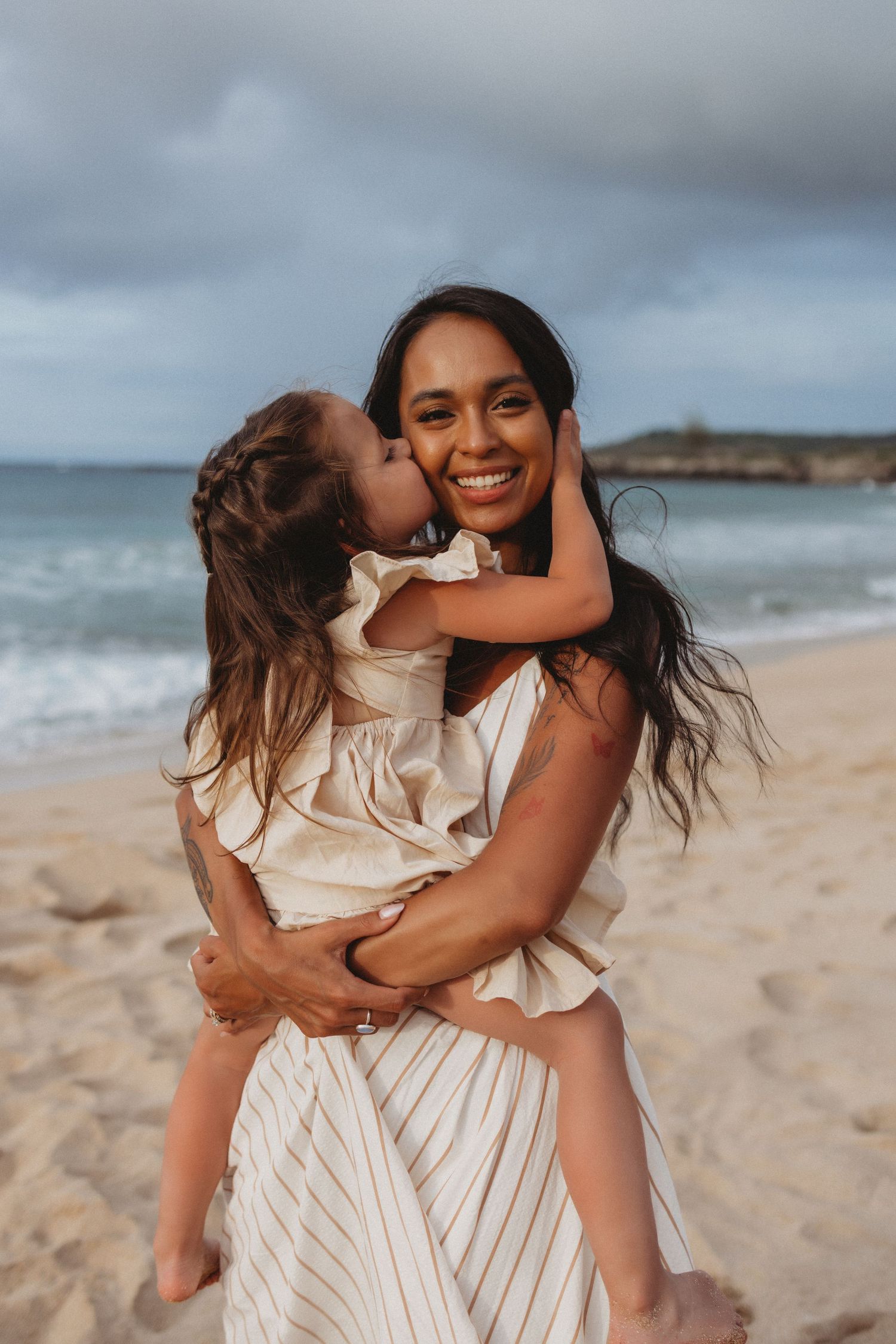 Maui family photography of daughter kissing mom on the beach at sunset.