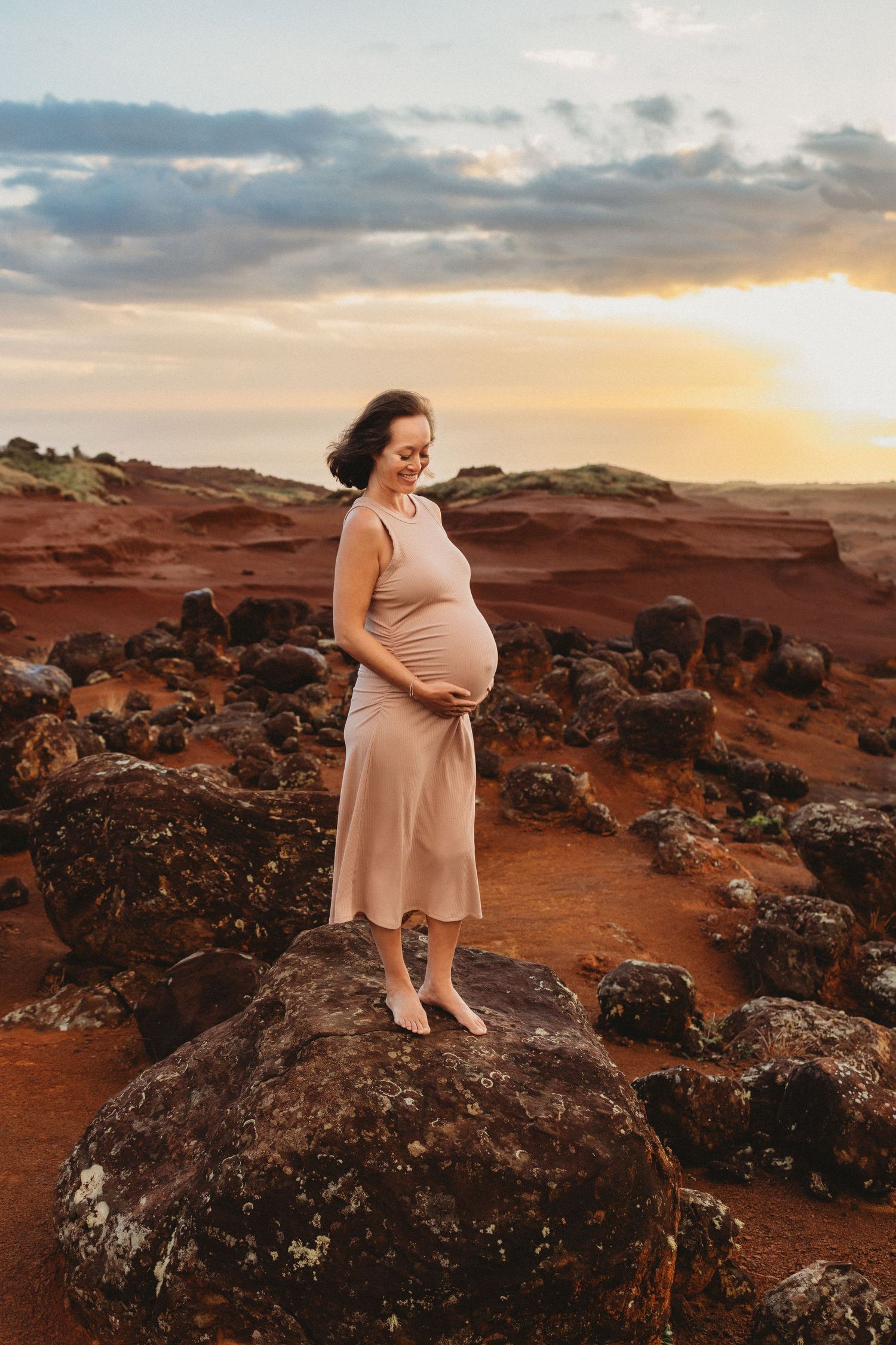 Maui maternity photography of pregnant woman standing on rocks at sunset.