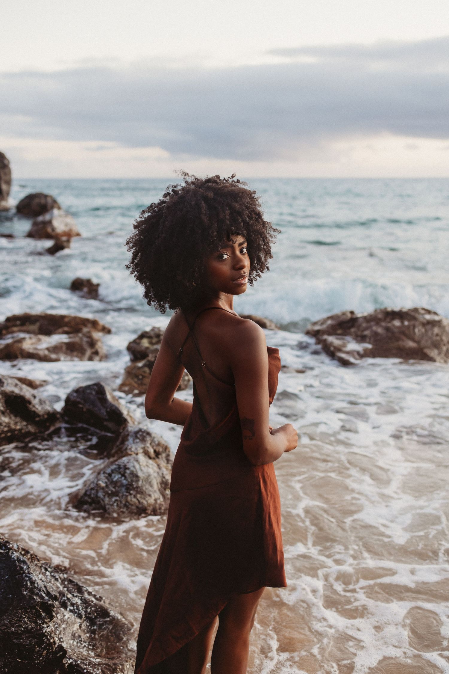 Lifestyle brand image featuring a woman posed on coastal rocks in the sea.