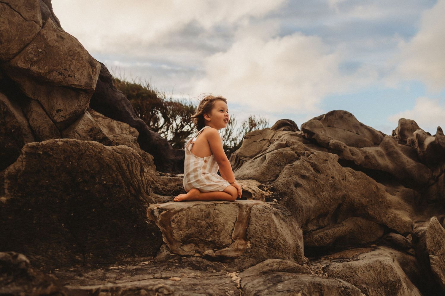 Maui lifestyle photography of a young boy sitting on coastal rocks.