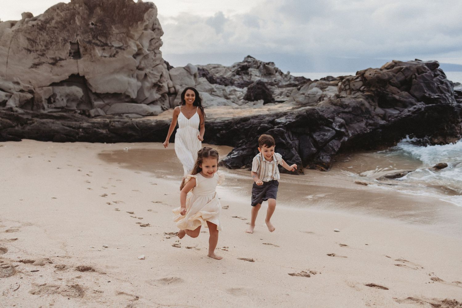 Family photo in Maui featuring mom and children running together on the beach.