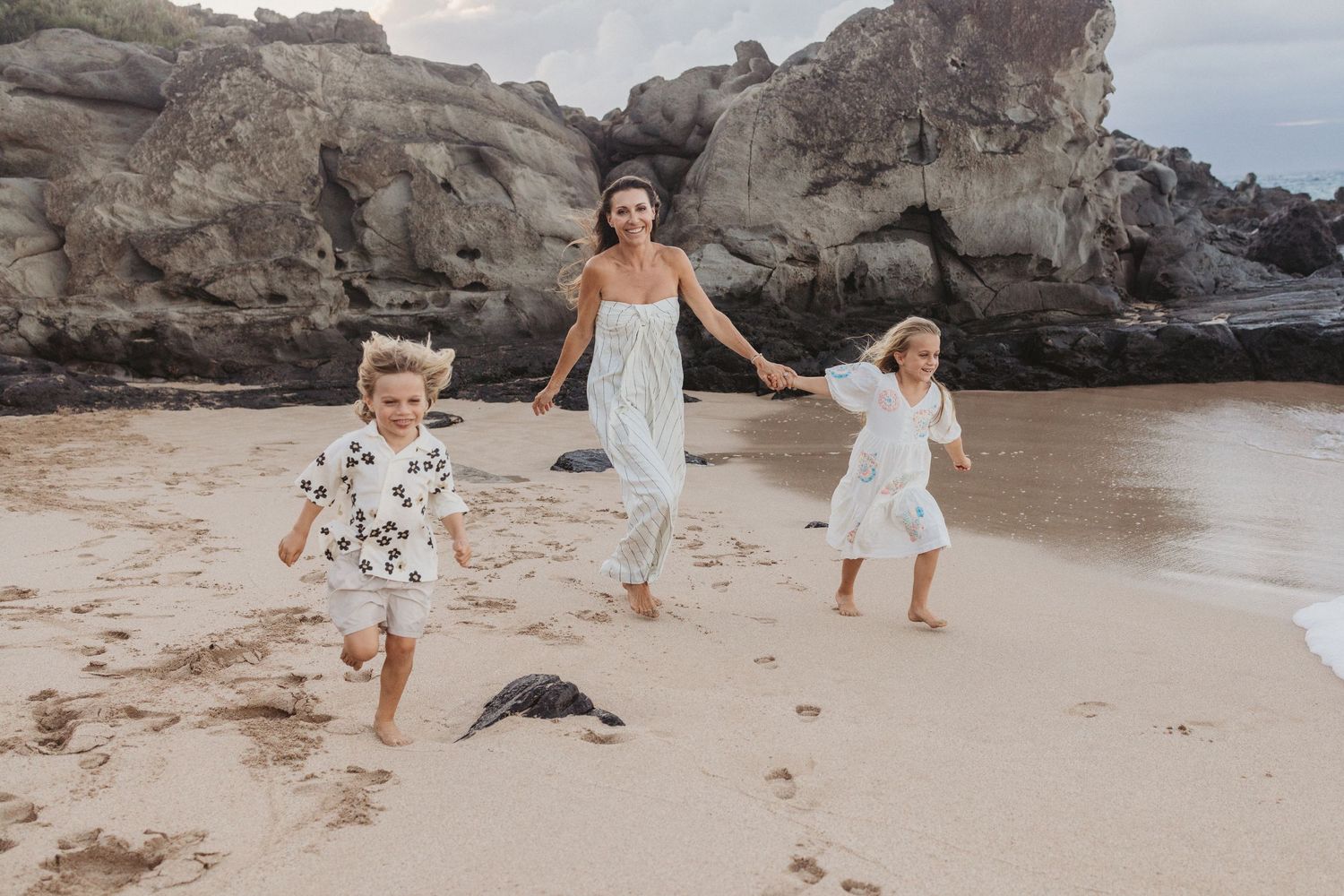 Family photo in Maui featuring mom and children running together on the beach.