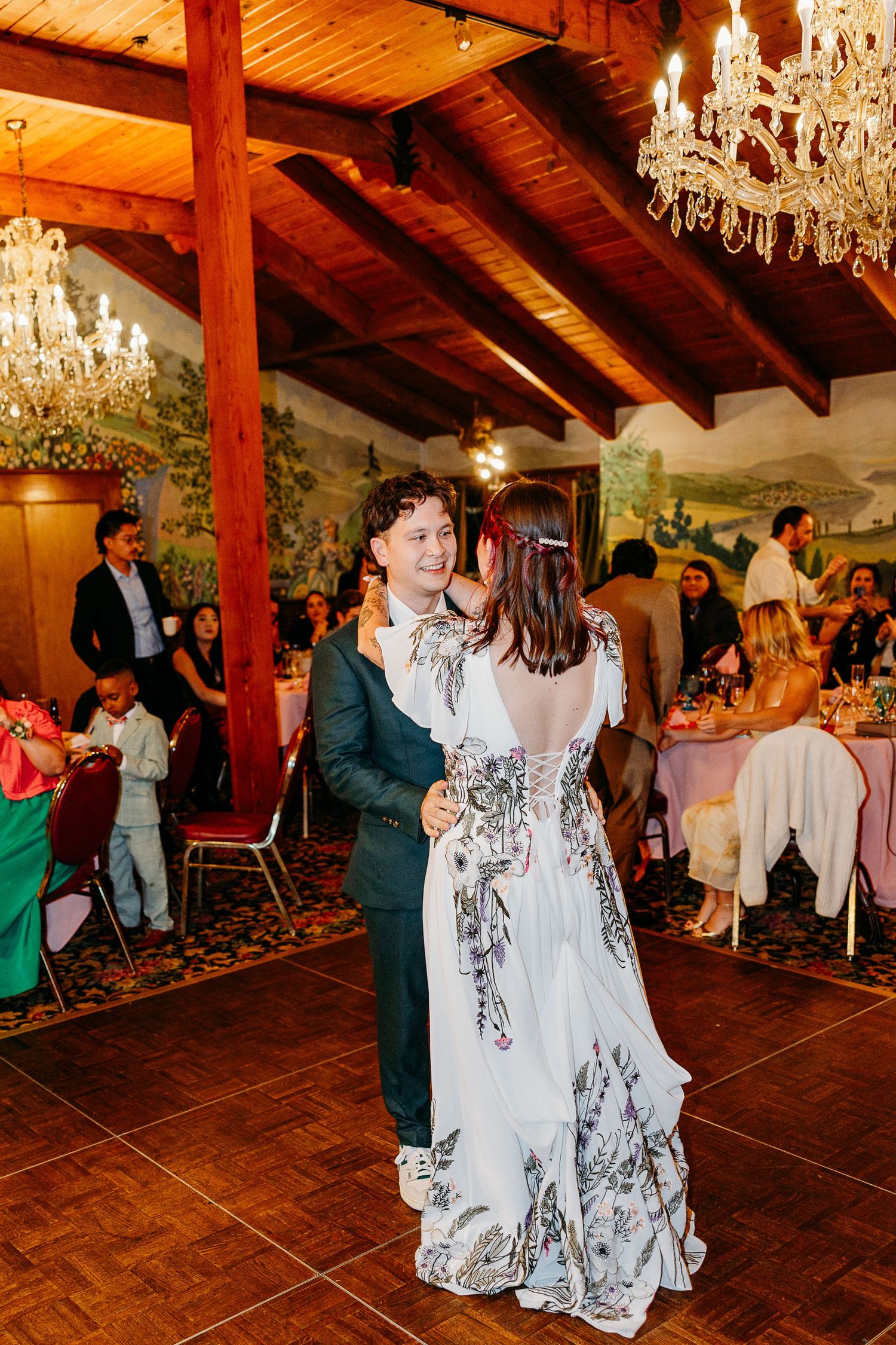 Wedding reception dance in rustic venue with wooden beams and chandeliers.