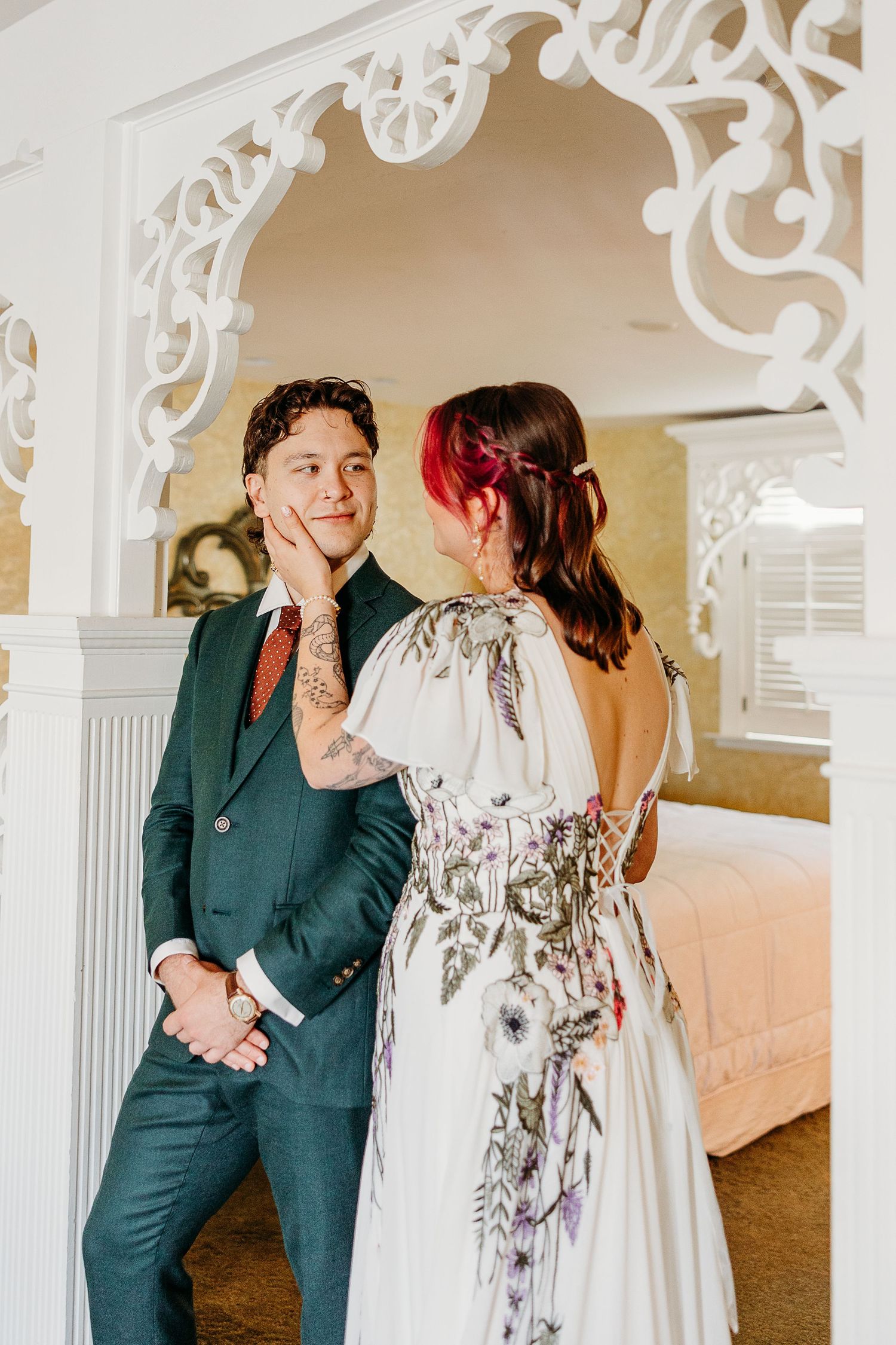 A couple shares a tender moment in formal attire, with ornate white architectural details in the background.