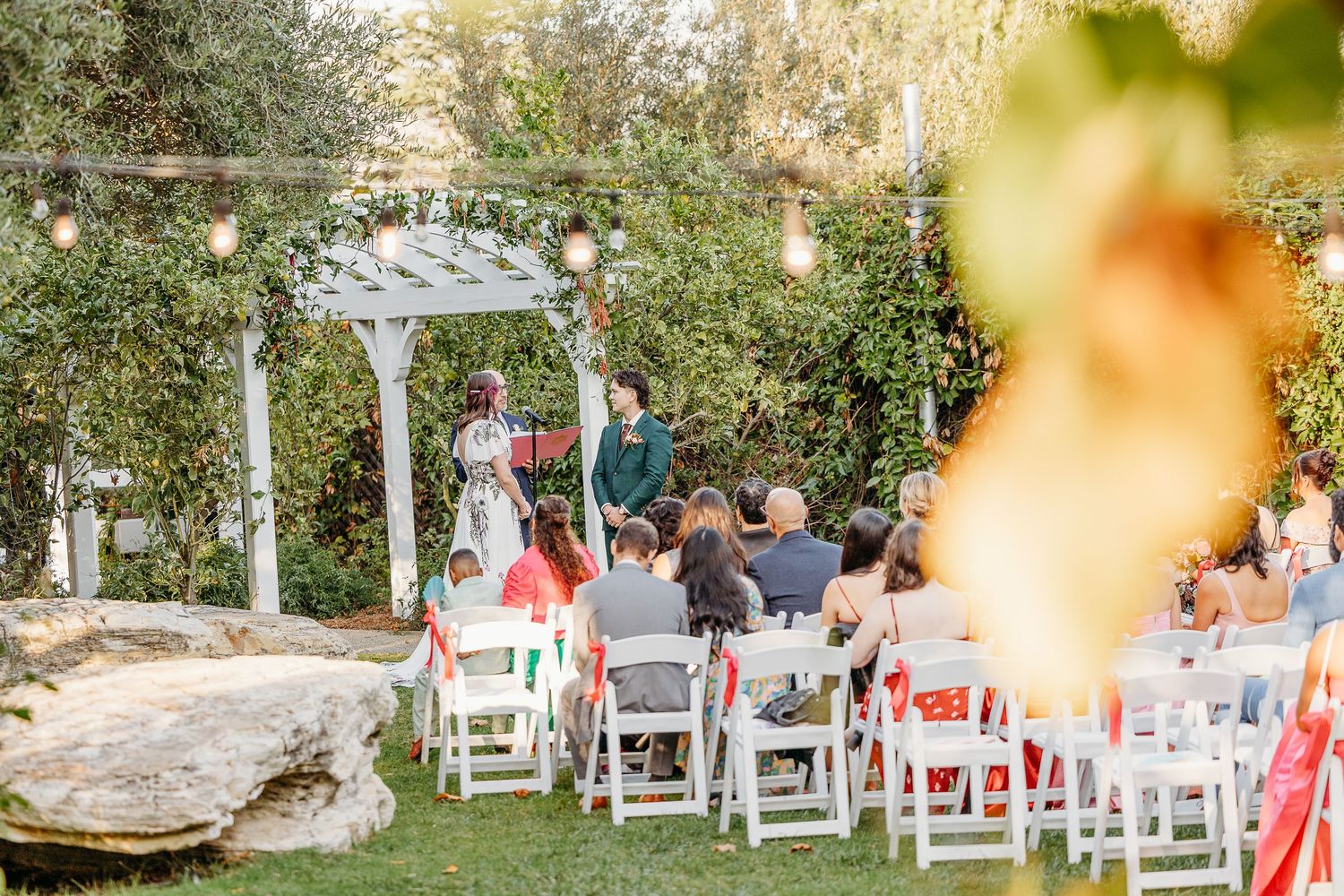 Outdoor wedding venue setup with white chairs and natural garden backdrop.