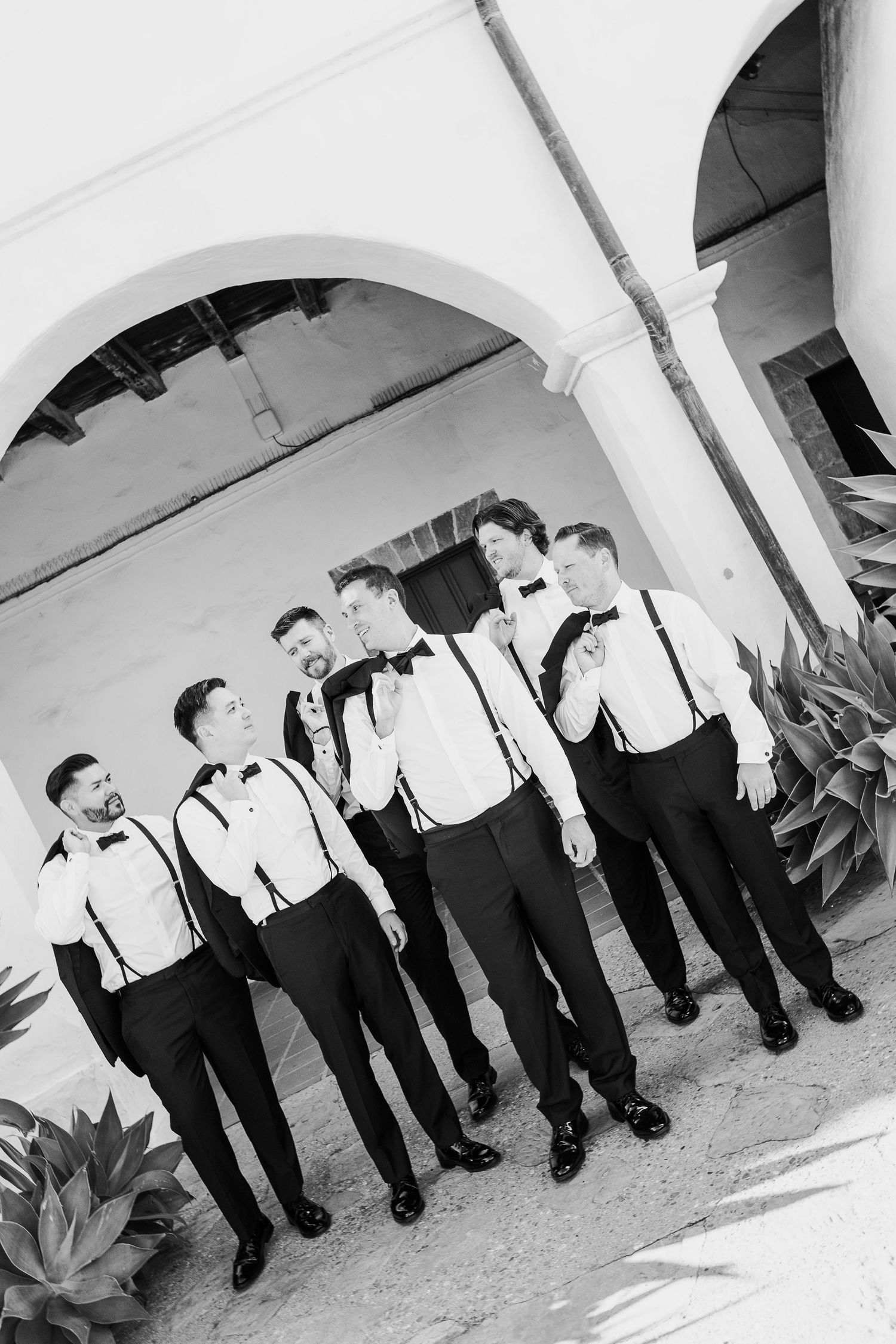 Black and white photo series of groomsmen lined up in formal attire under arched walkway.