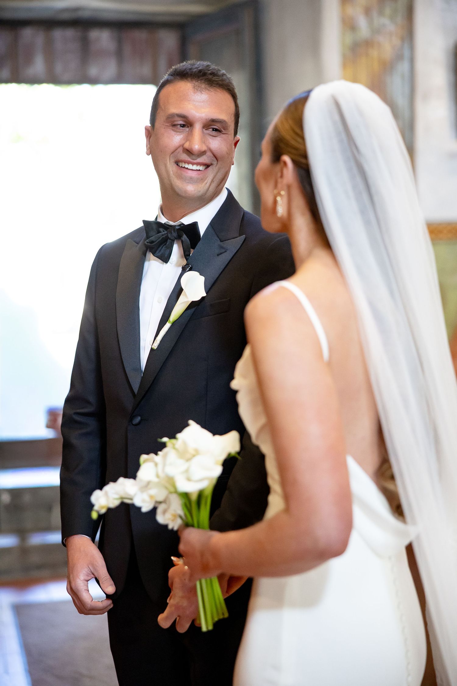 A joyful wedding moment as the couple shares their first look, with the bride holding a white calla lily bouquet.