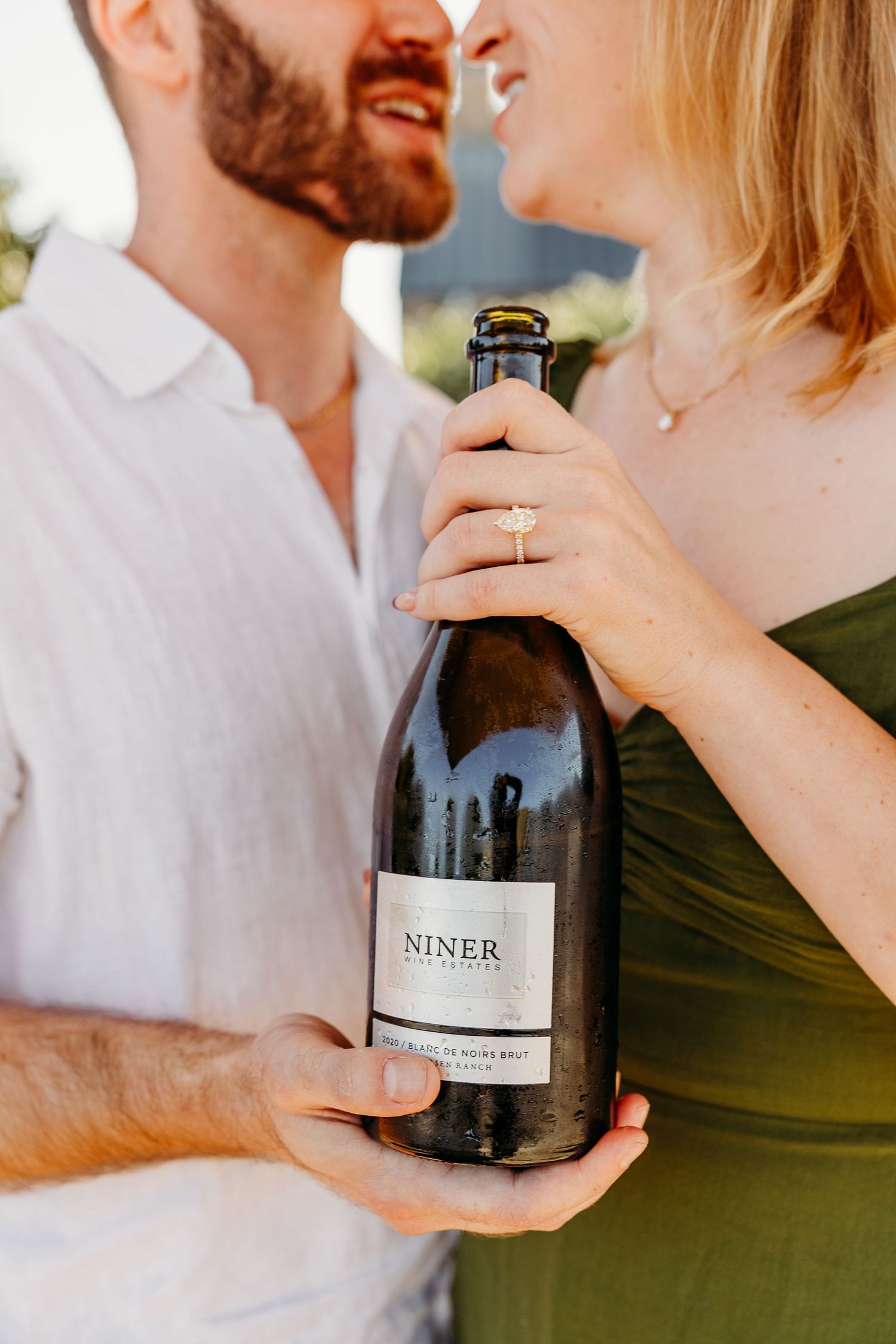 Couple shares intimate moment while holding wine bottles during golden hour photoshoot.