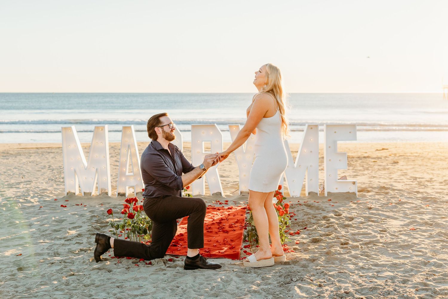 Beach proposal setup with decorative letters and romantic decor during sunset.