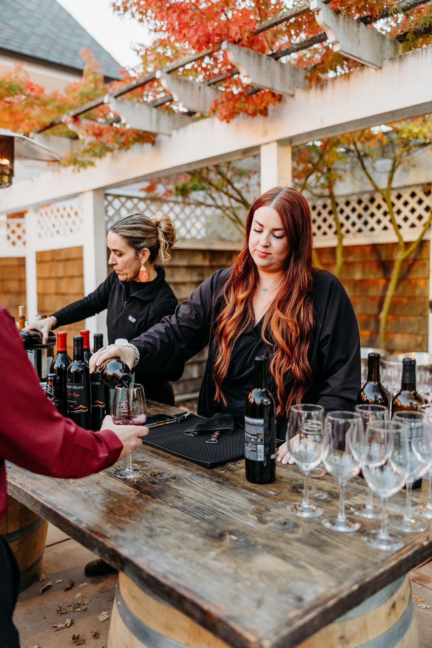 Bartender preparing drinks at rustic wooden bar under autumn foliage.