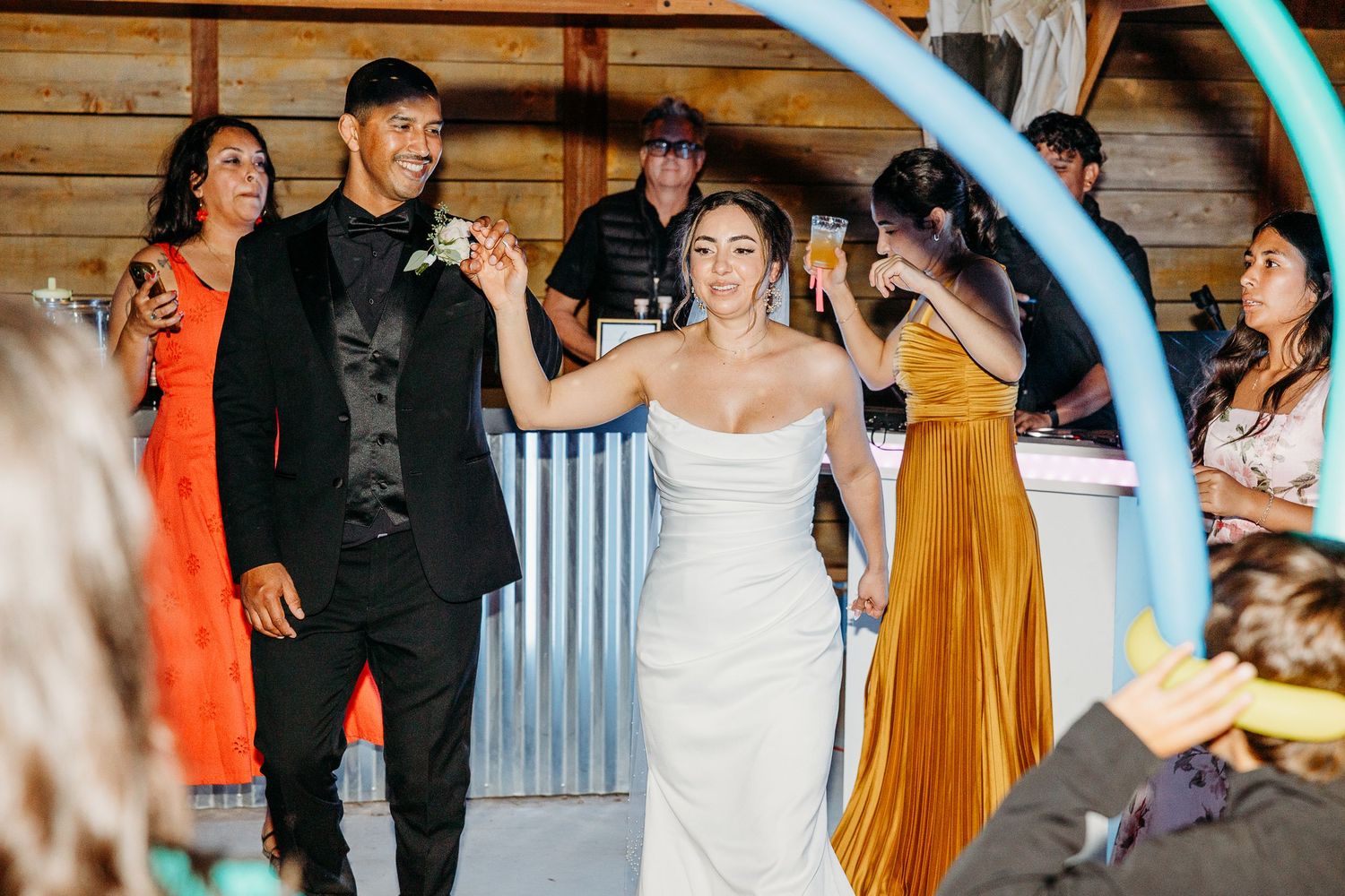 Wedding guests dancing and celebrating at indoor reception with colorful lighting.