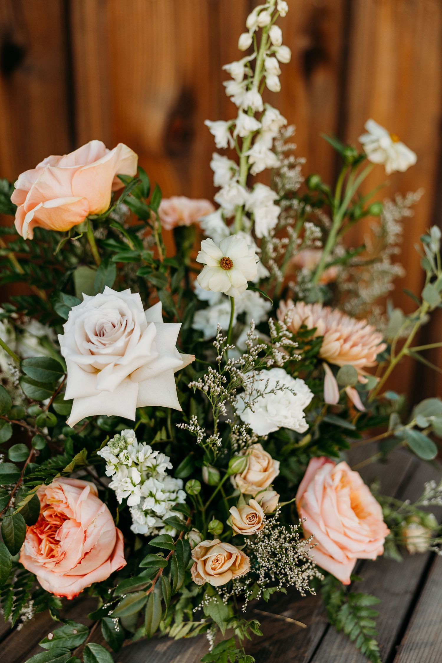 Elegant floral centerpiece with peach roses, white flowers and greenery arranged on dark wood surface.