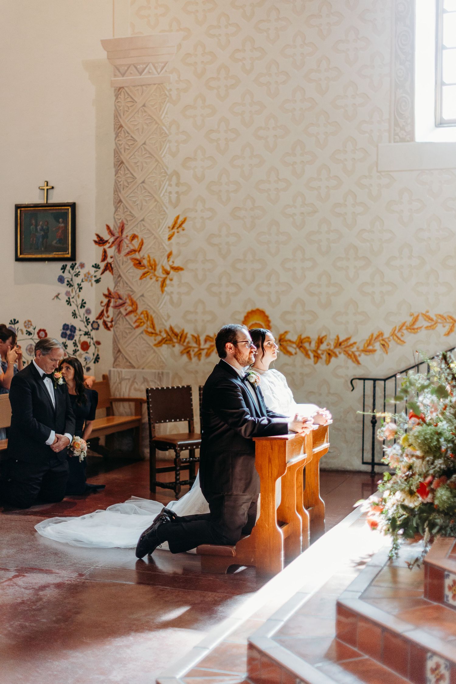 A church wedding ceremony with decorative wall details and floral arrangements int he historic SLO Mission.