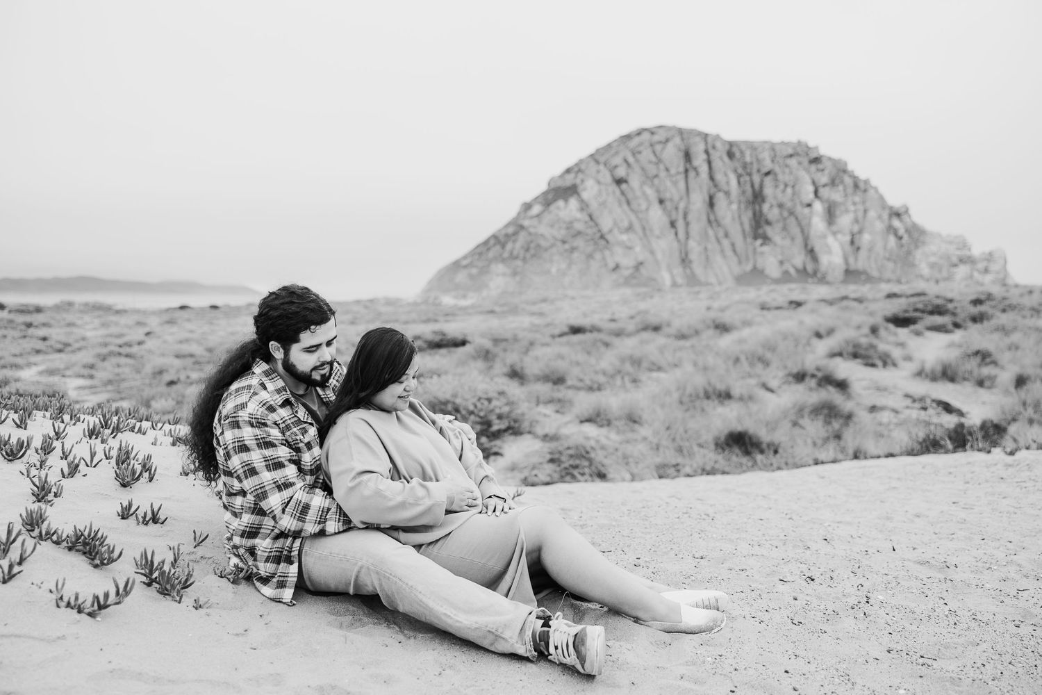 A couple rests together on sandy ground with a majestic mountain formation visible in the distance.