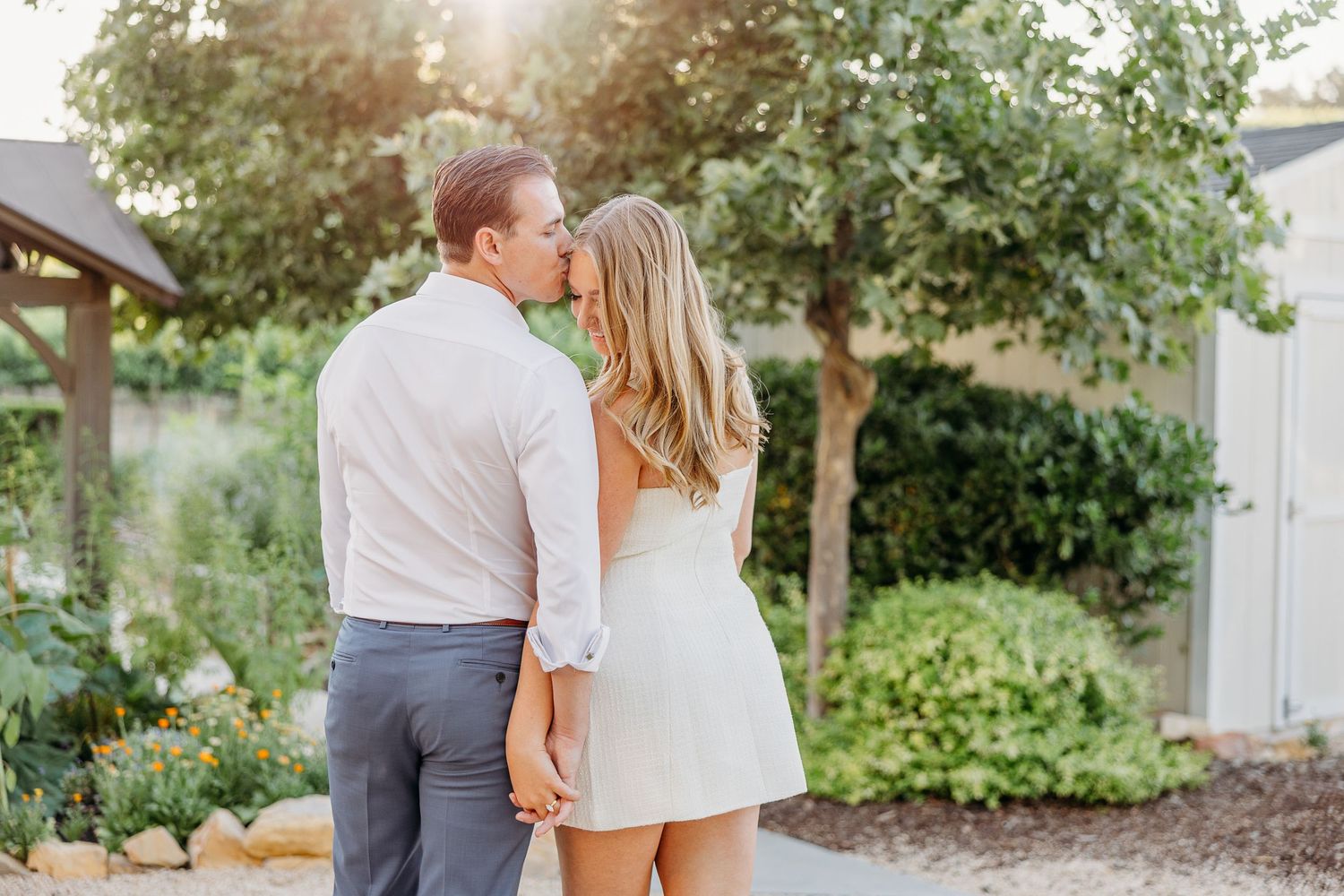 Couple embraces in a romantic outdoor garden setting with lush greenery and natural lighting.
