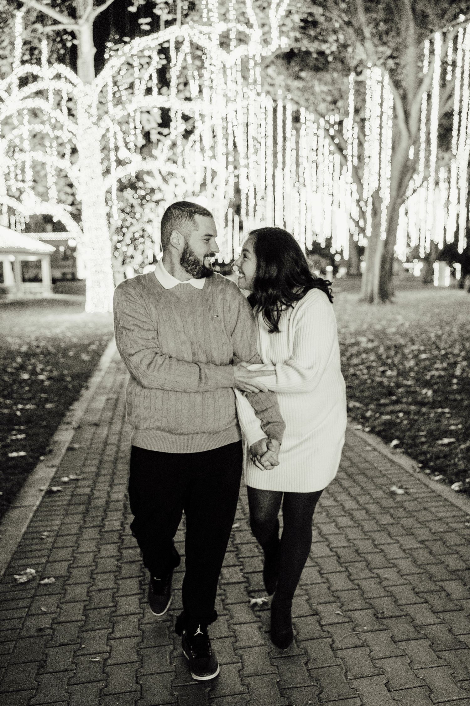 Black and white photo series showing two people walking together on a brick path through a tree-lined park.