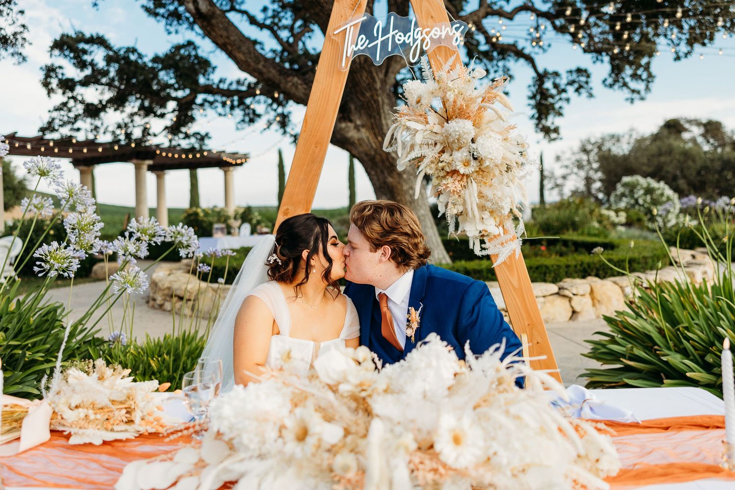 Romantic moment between newlyweds at their reception table decorated with pampas grass and orange accents.