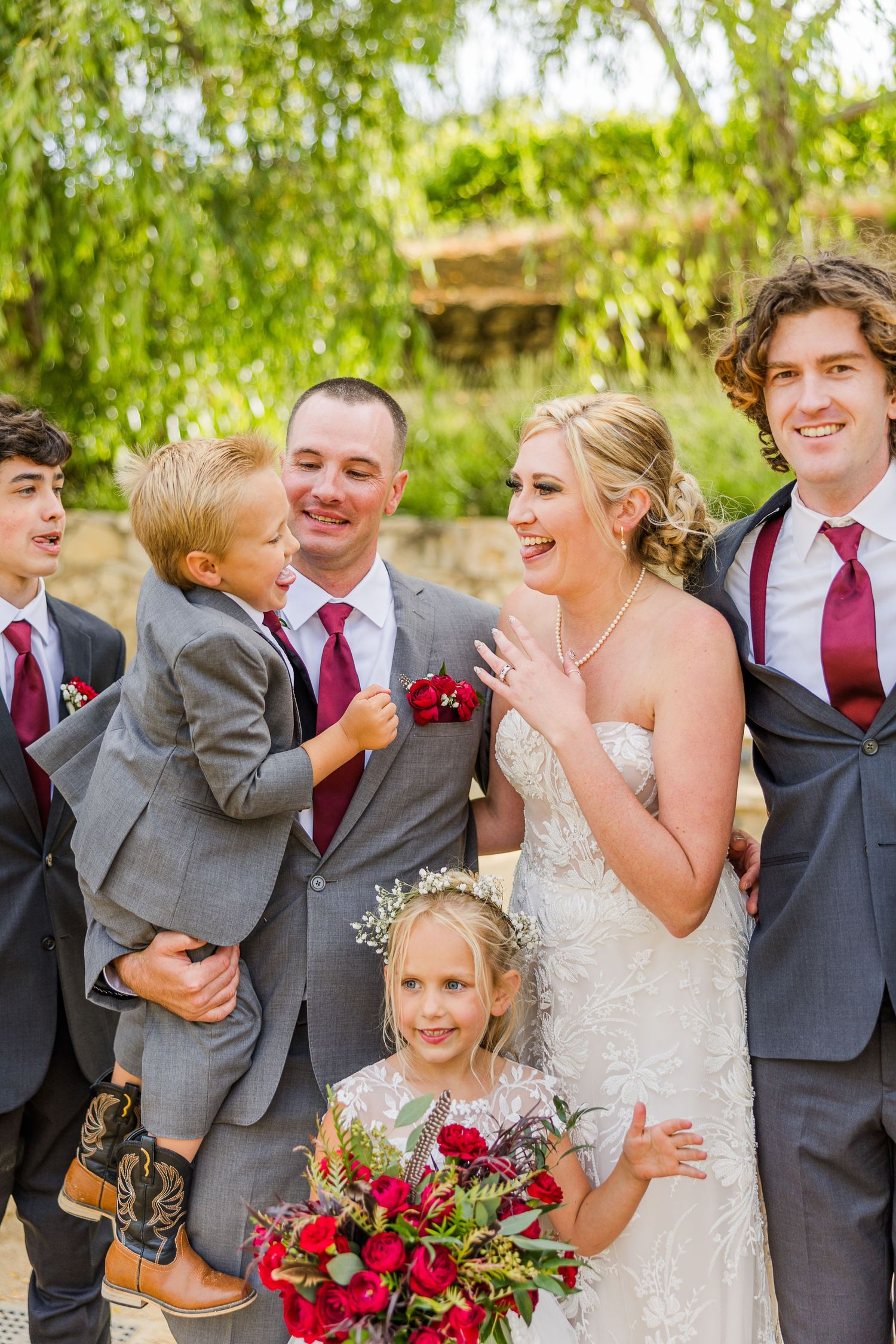 Candid moment with wedding party members and young attendants holding red bouquets.