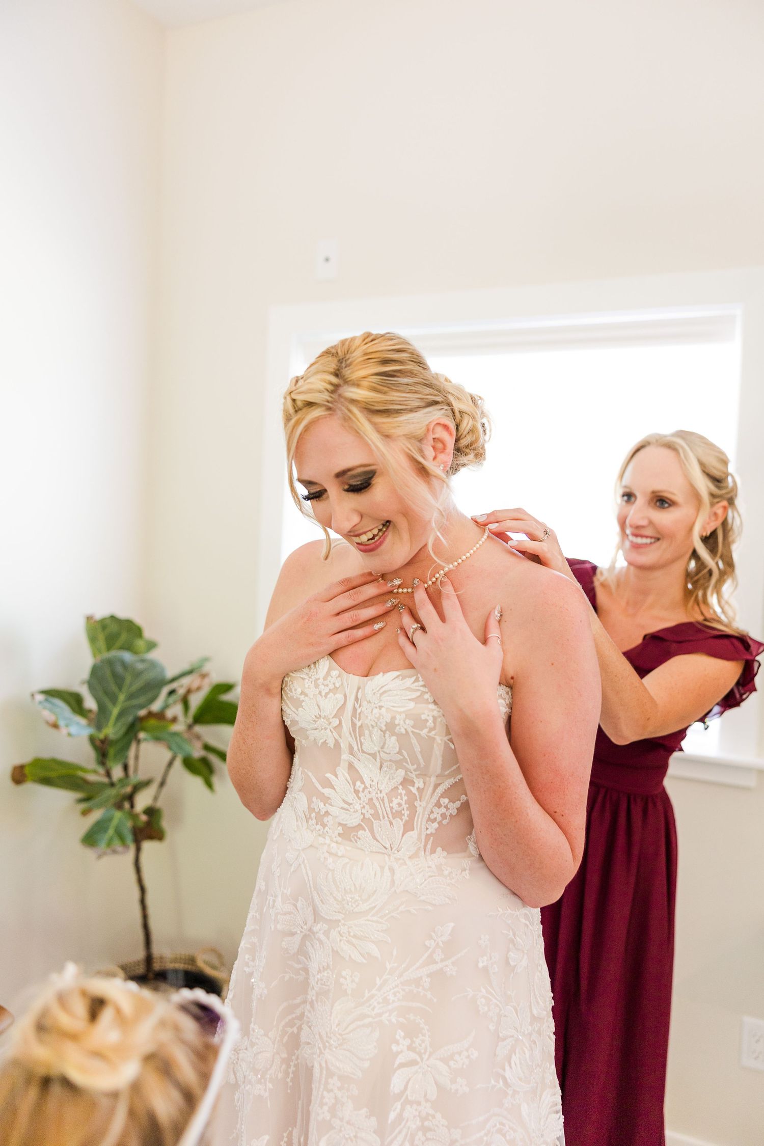 Emotional bride wearing pearls touches her neck while getting ready in white lace wedding dress.