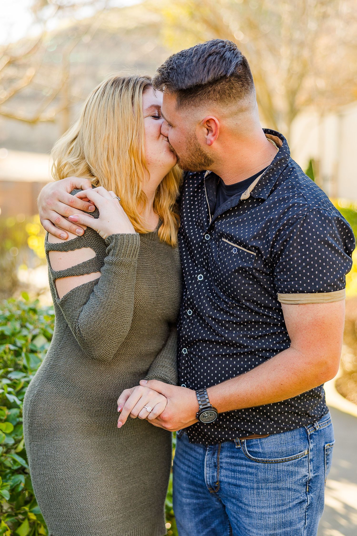 Intimate moment between couple kissing in sunny garden with polka dot shirt and sweater dress.