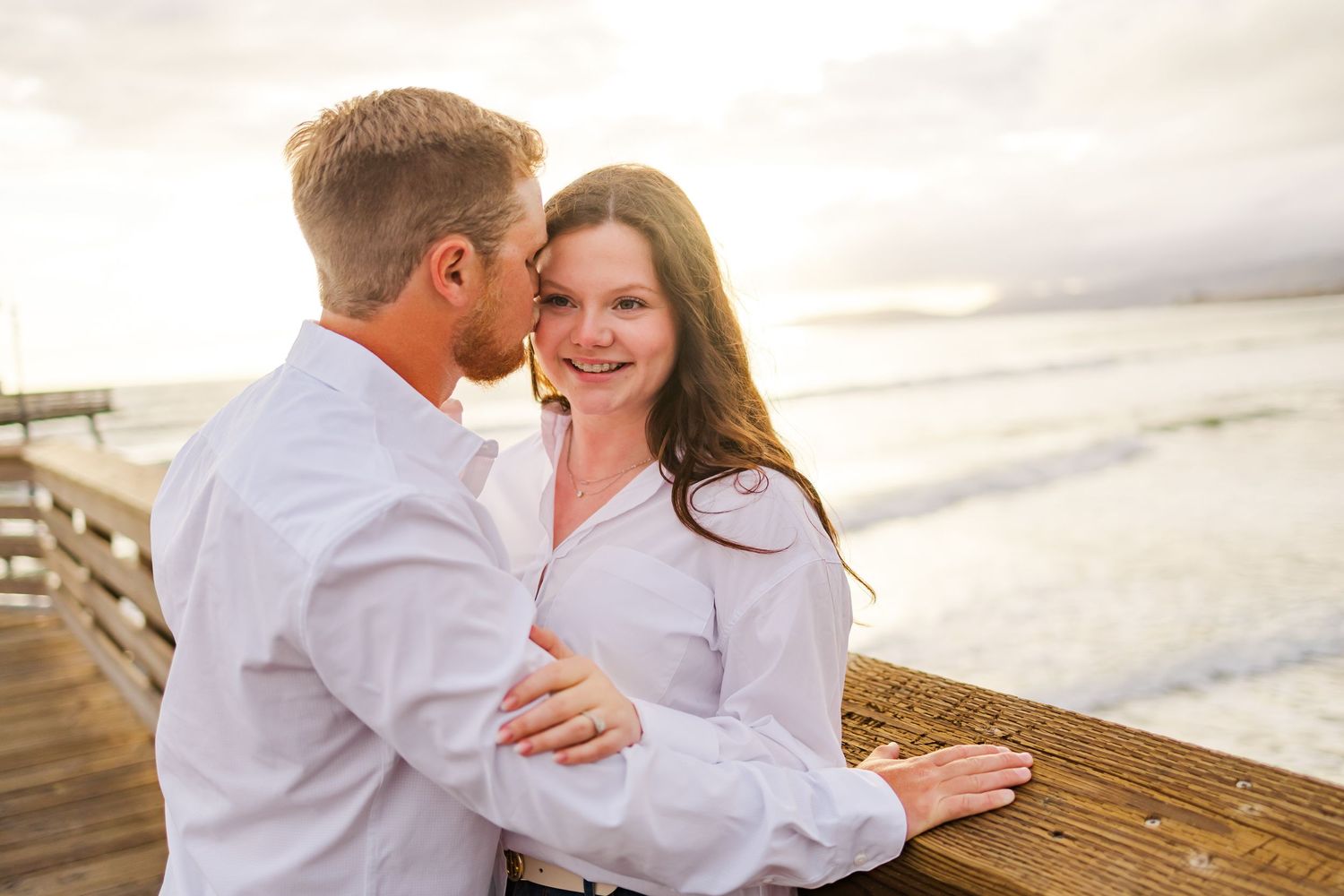 A romantic couple sharing an intimate moment on a pier during golden hour.