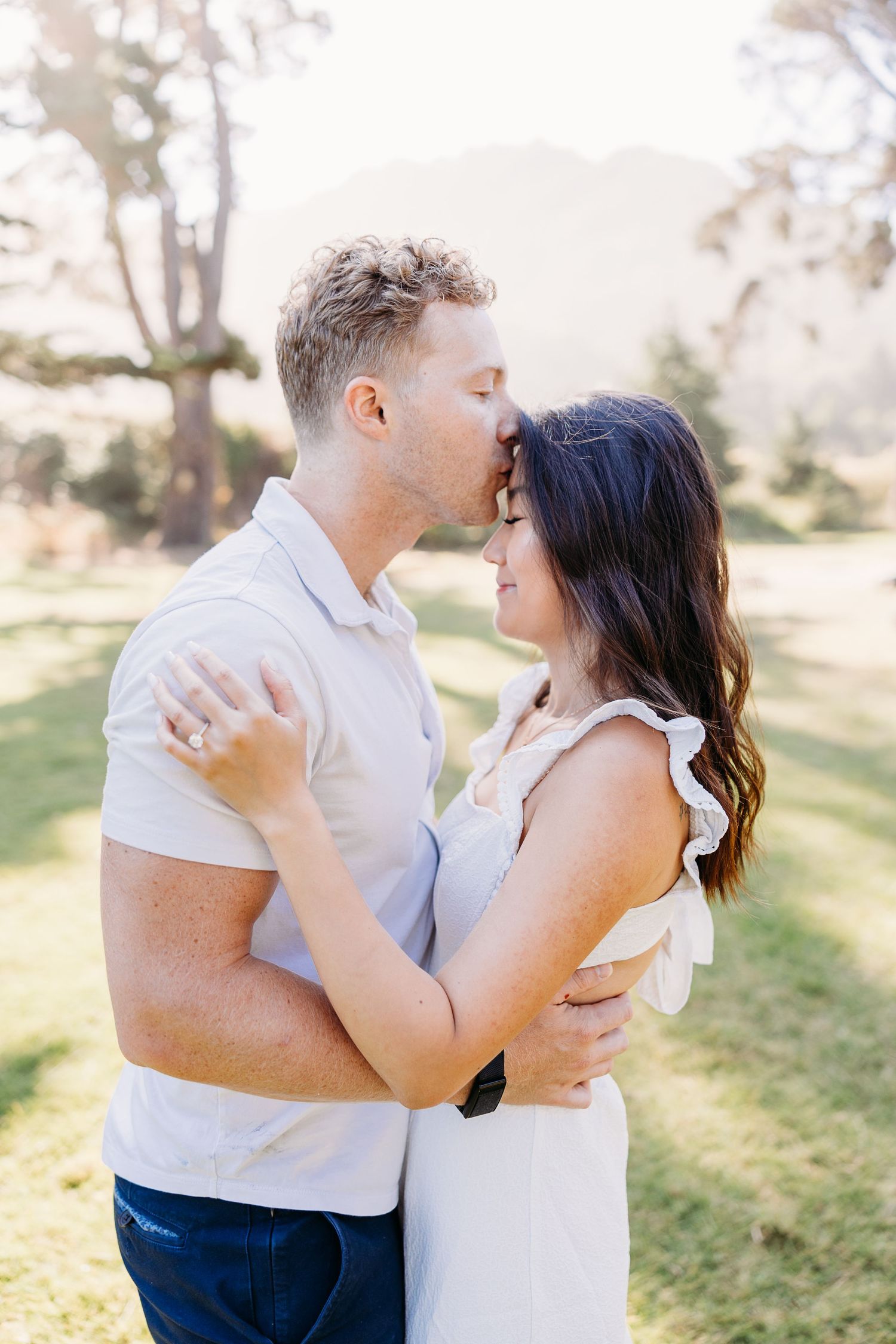Romantic outdoor engagement photo of couple in matching white outfits.