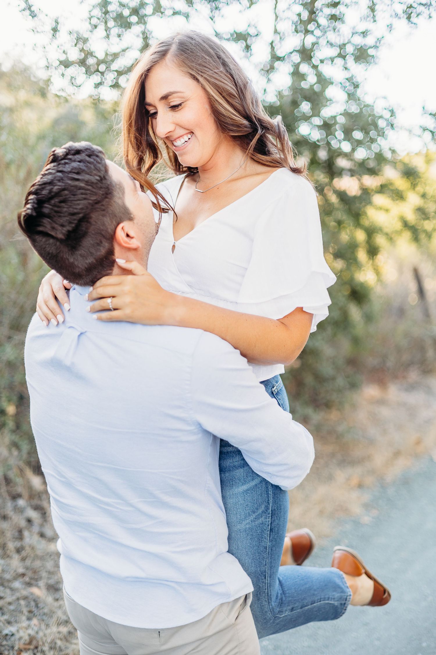 A joyful couple embracing on a nature trail with warm sunlight filtering through trees.