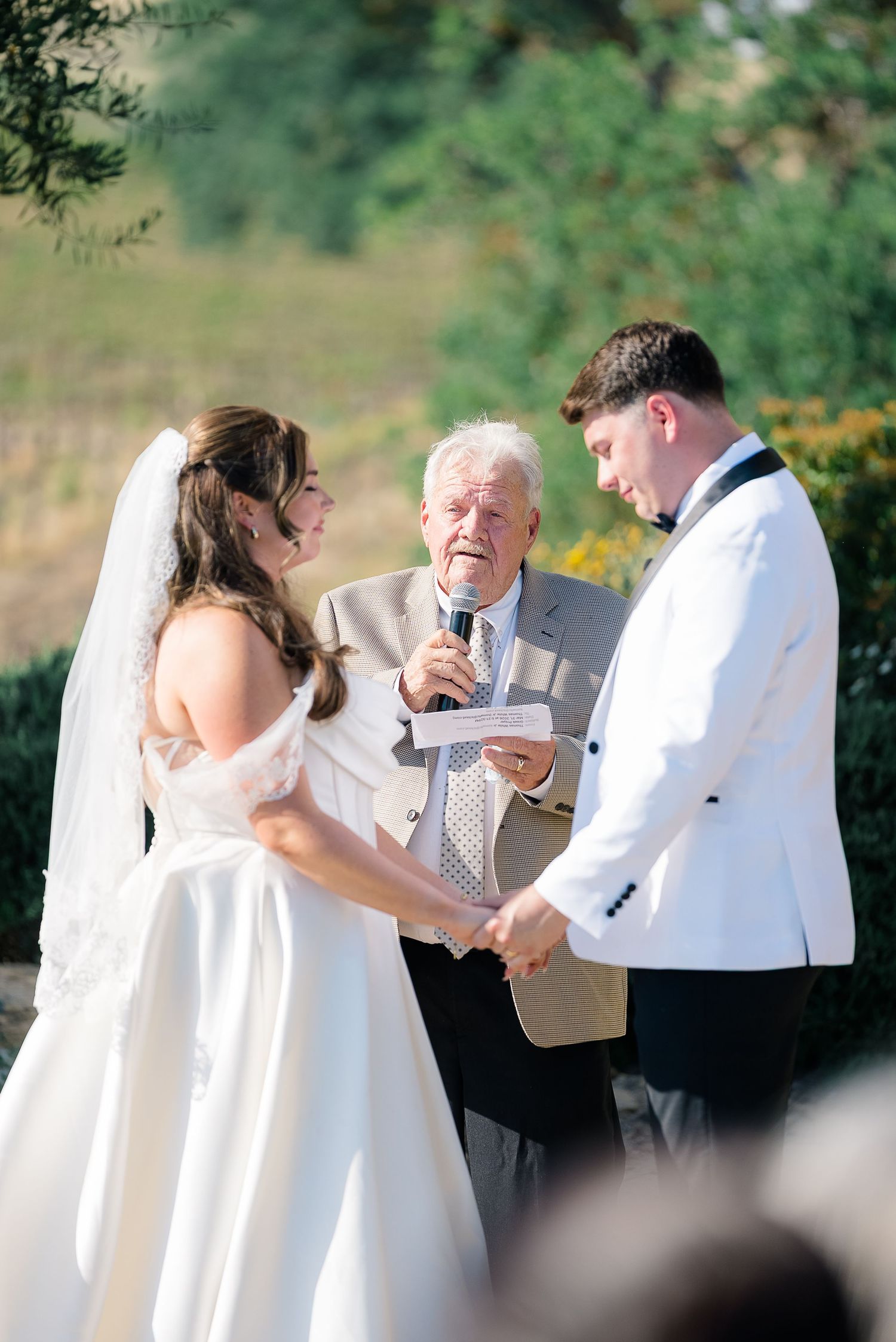 Bride and groom holding hands during outdoor wedding ceremony with officiant.