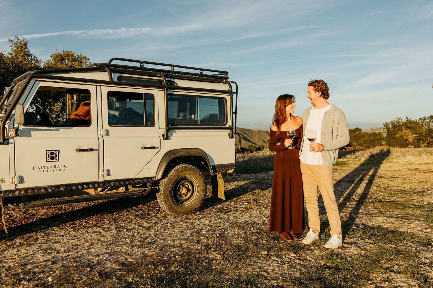A vintage Land Rover sits against a dramatic mountain backdrop during golden hour.