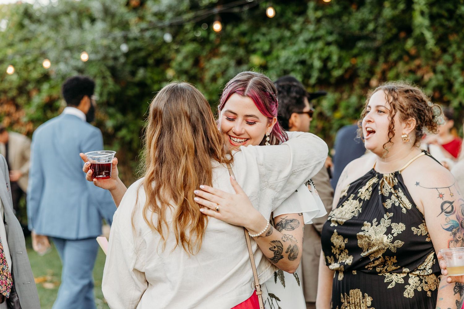 Wedding guests celebrate outdoors under string lights during a joyful reception gathering.