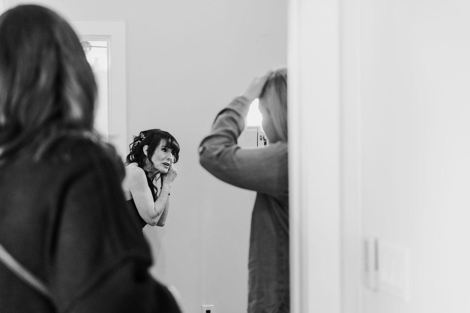A person looks into a mirror while styling their hair in a black and white photograph.