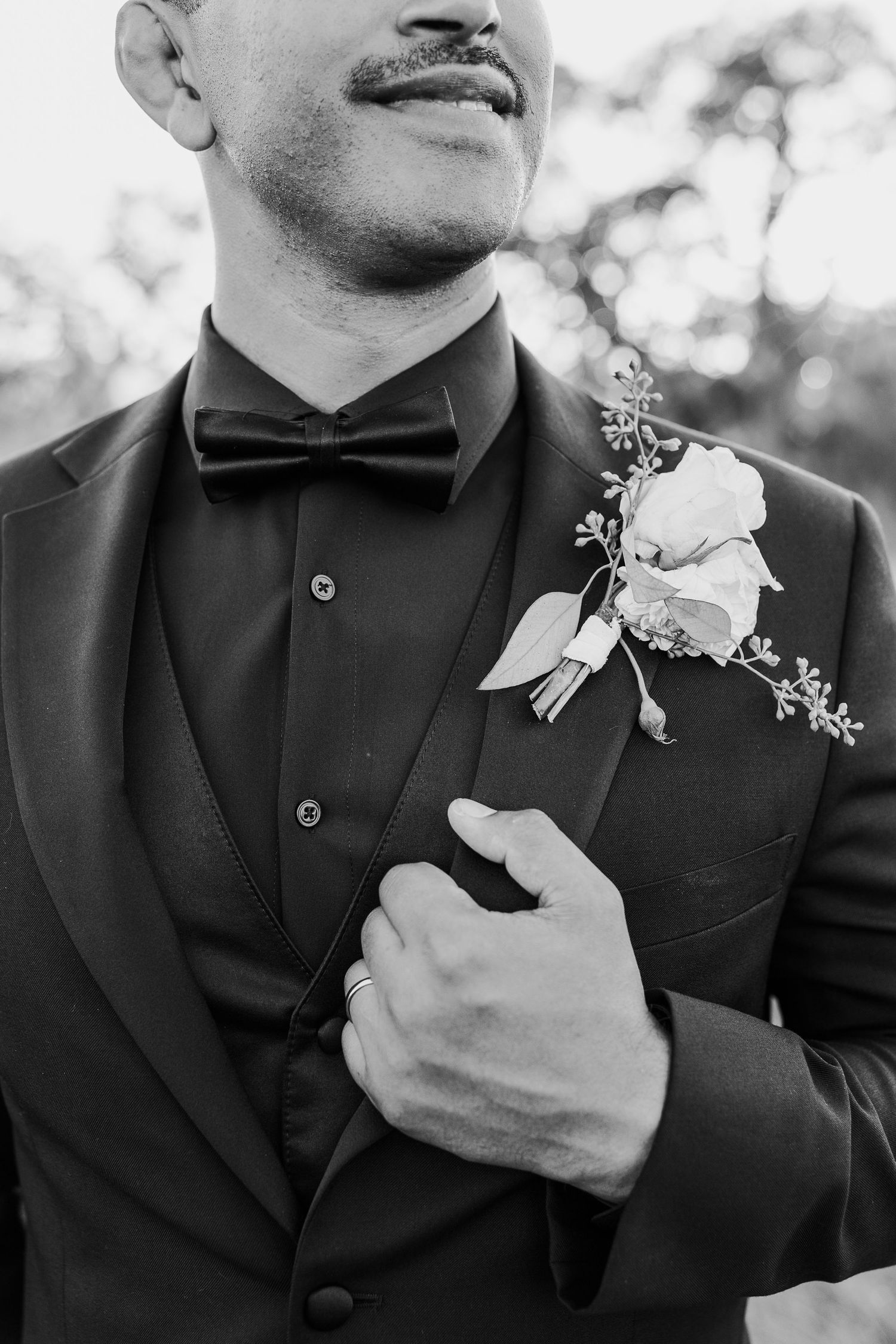 Close-up details of groom's formal attire showing white boutonniere and black bow tie.