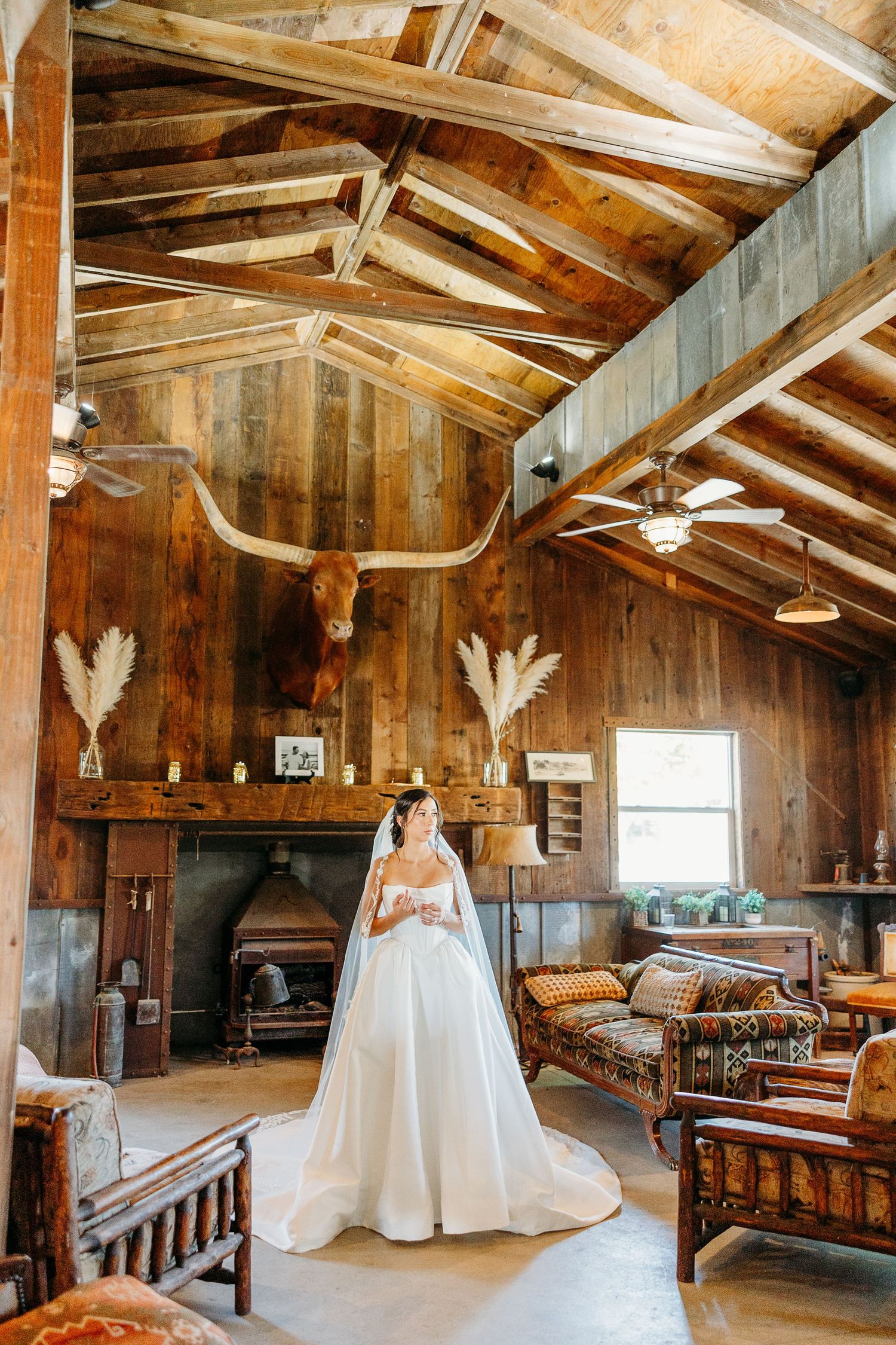 Rustic wooden barn interior with exposed beams, white wedding dresses displayed, and vintage furniture creating a charming venue.