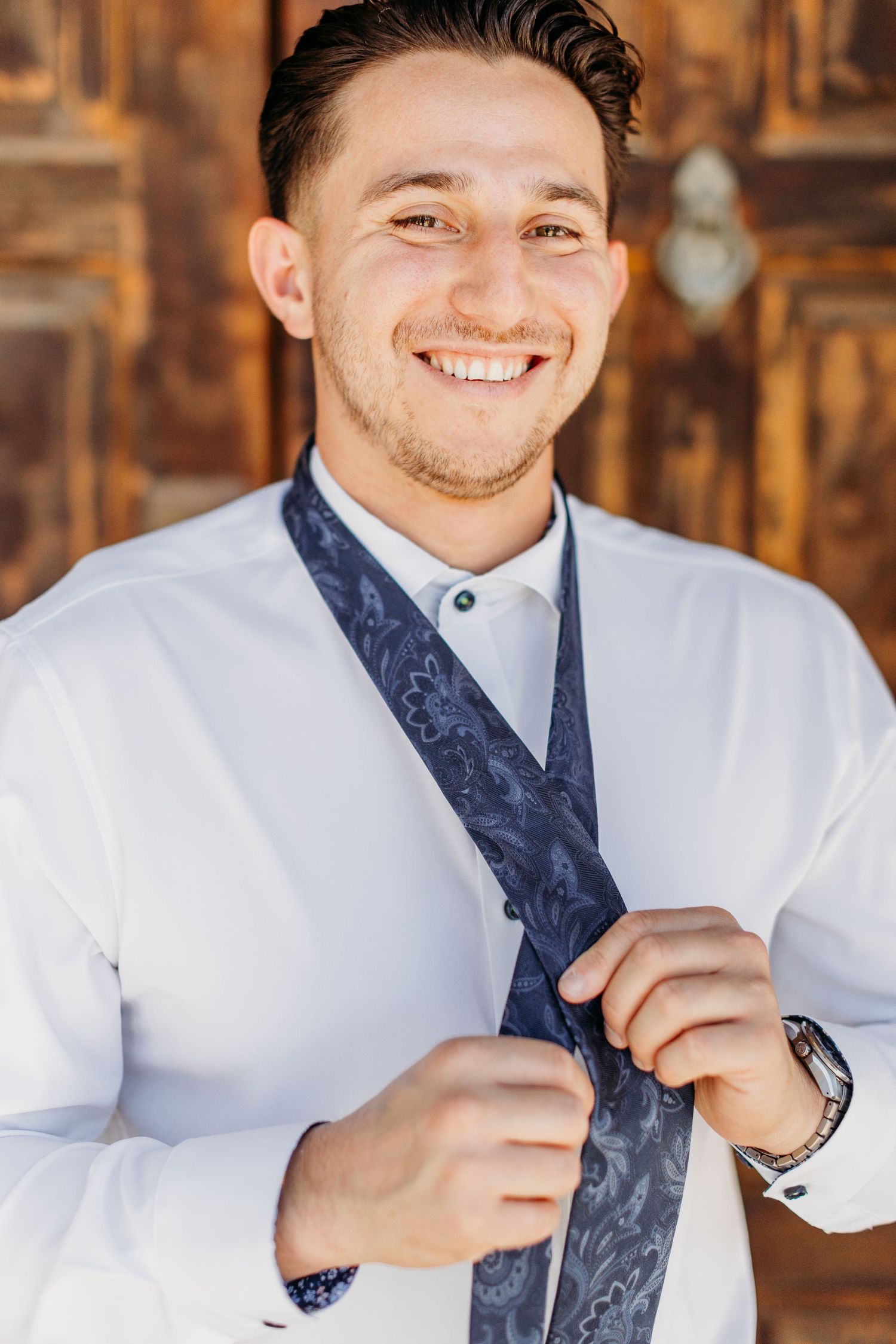 A sequence showing someone adjusting a navy patterned tie while wearing a crisp white dress shirt.