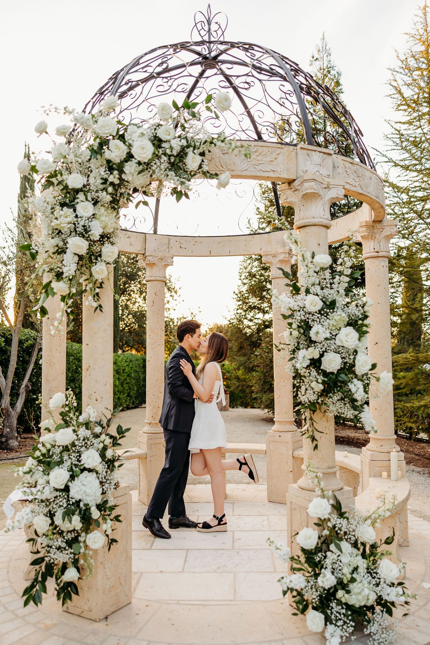 Romantic sequence in a white gazebo adorned with cascading white flowers and greenery.