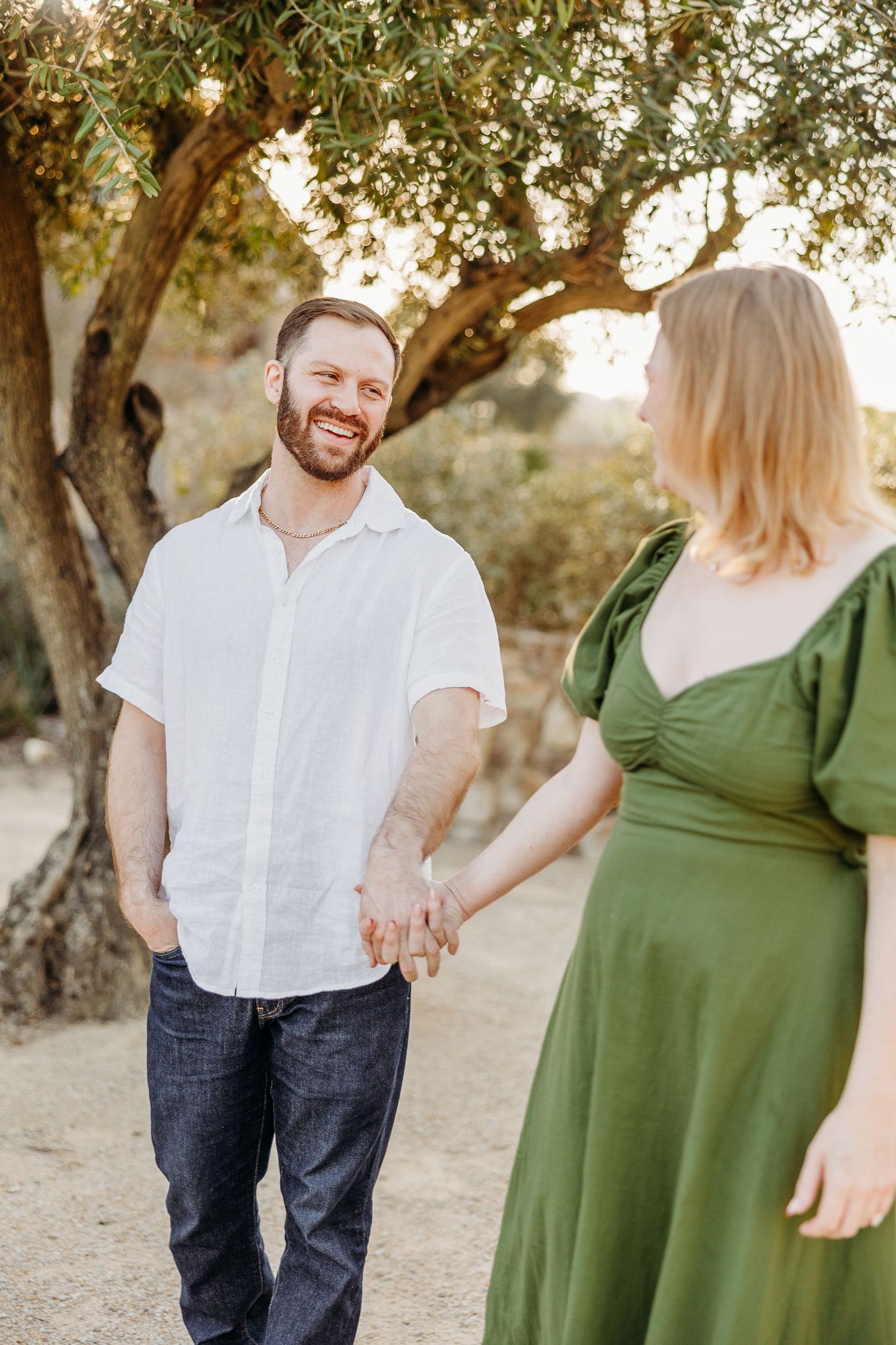 A couple shares tender moments among olive trees during a golden hour photoshoot.