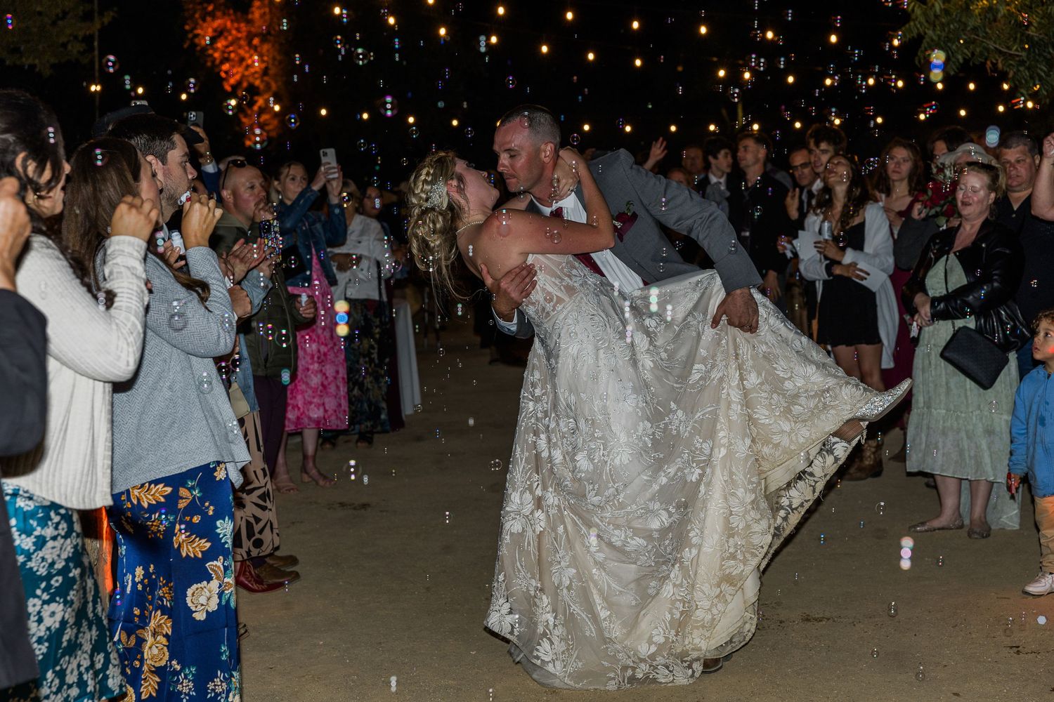 Groom lifts bride during romantic dance finale as guests cheer with sparklers.