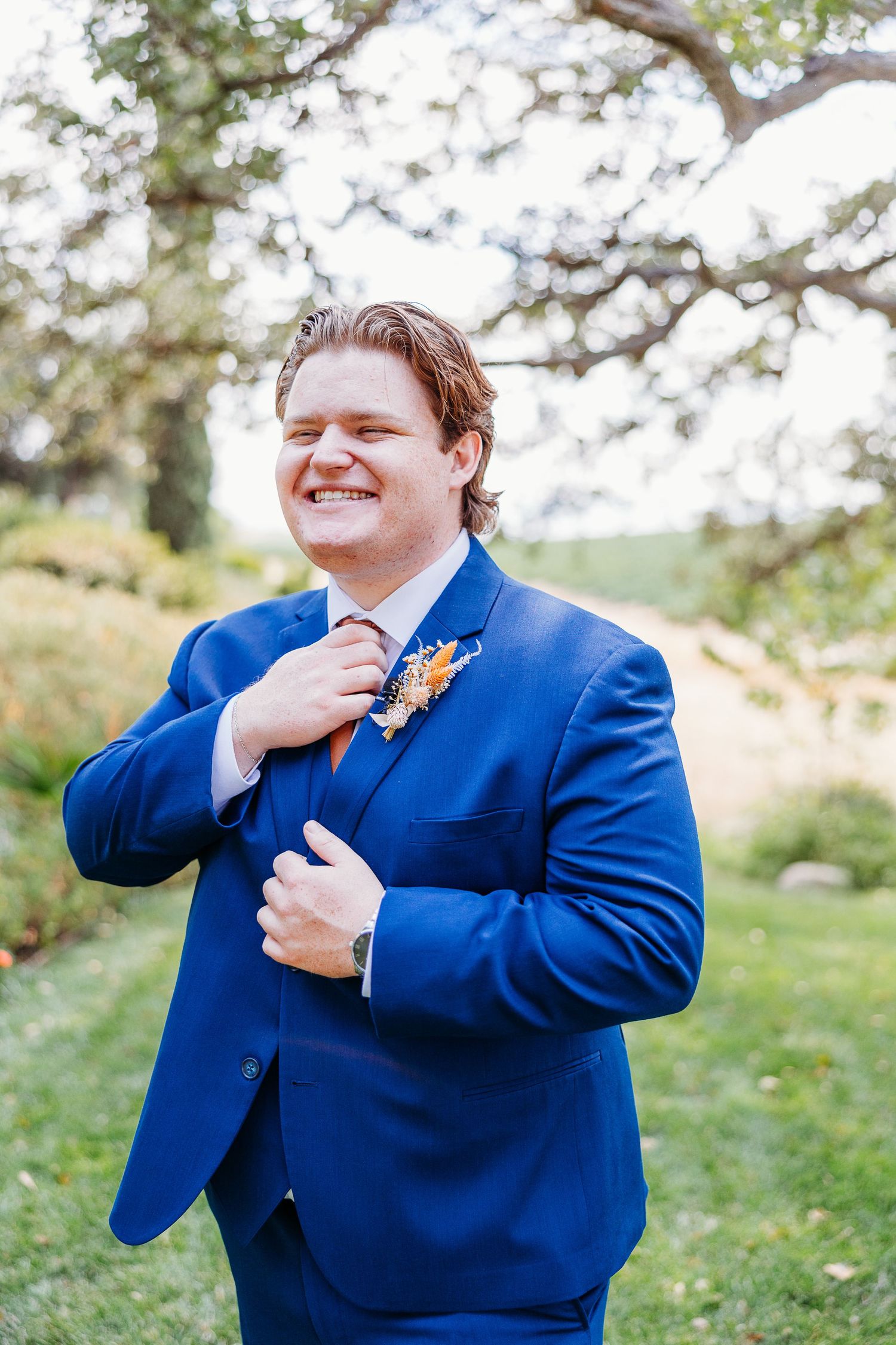 A happy person in bright blue suit laughs while adjusting their collar outdoors.