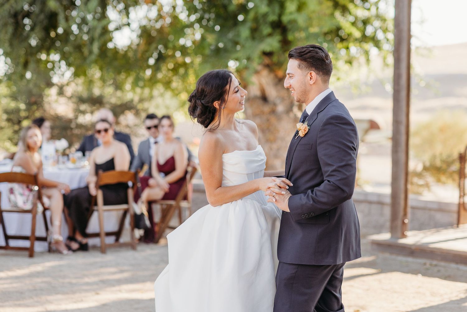 Wedding guests enjoying an outdoor celebration under trees at a scenic venue.