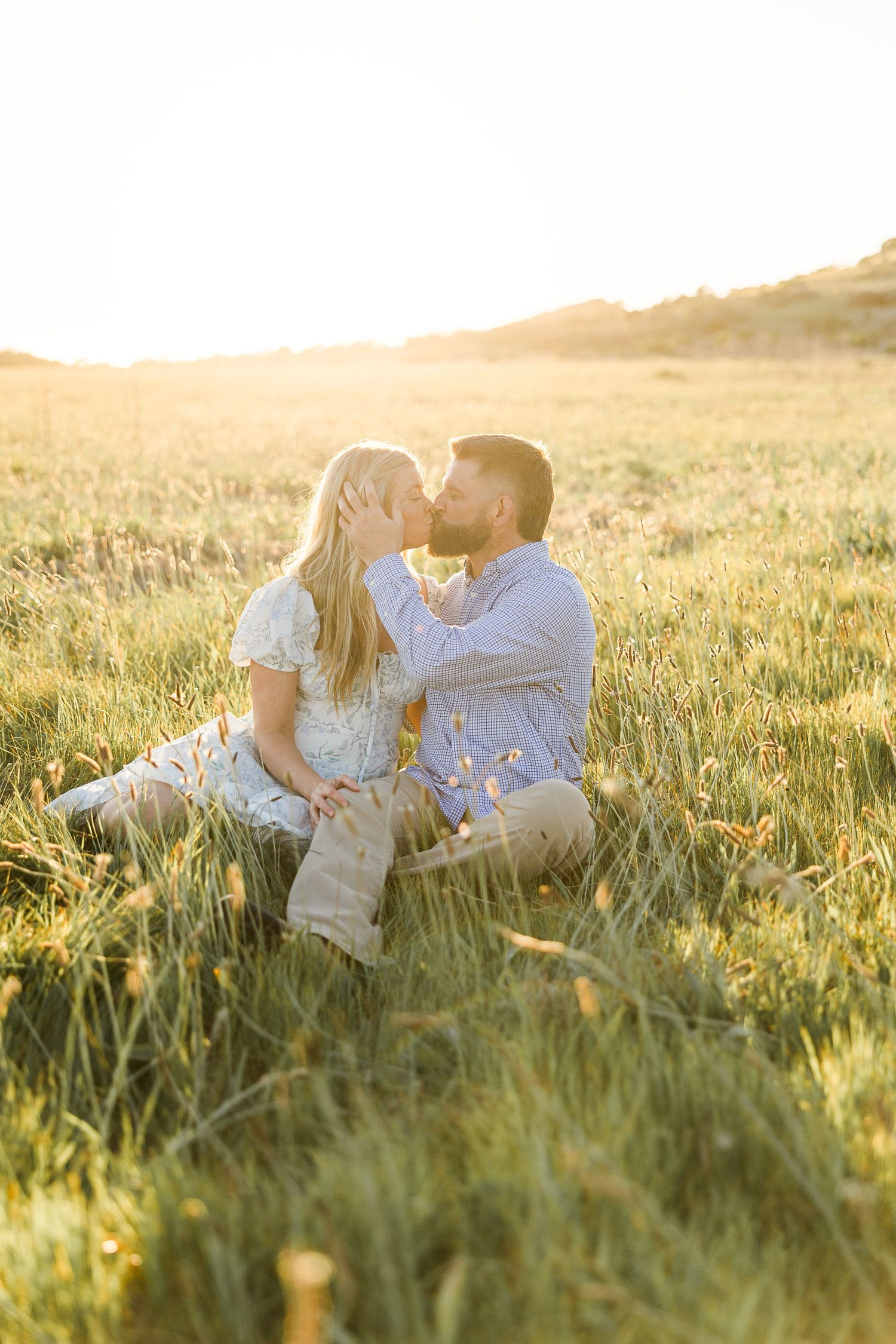 Couple lounges together in tall grass during sunset in scenic California hills.