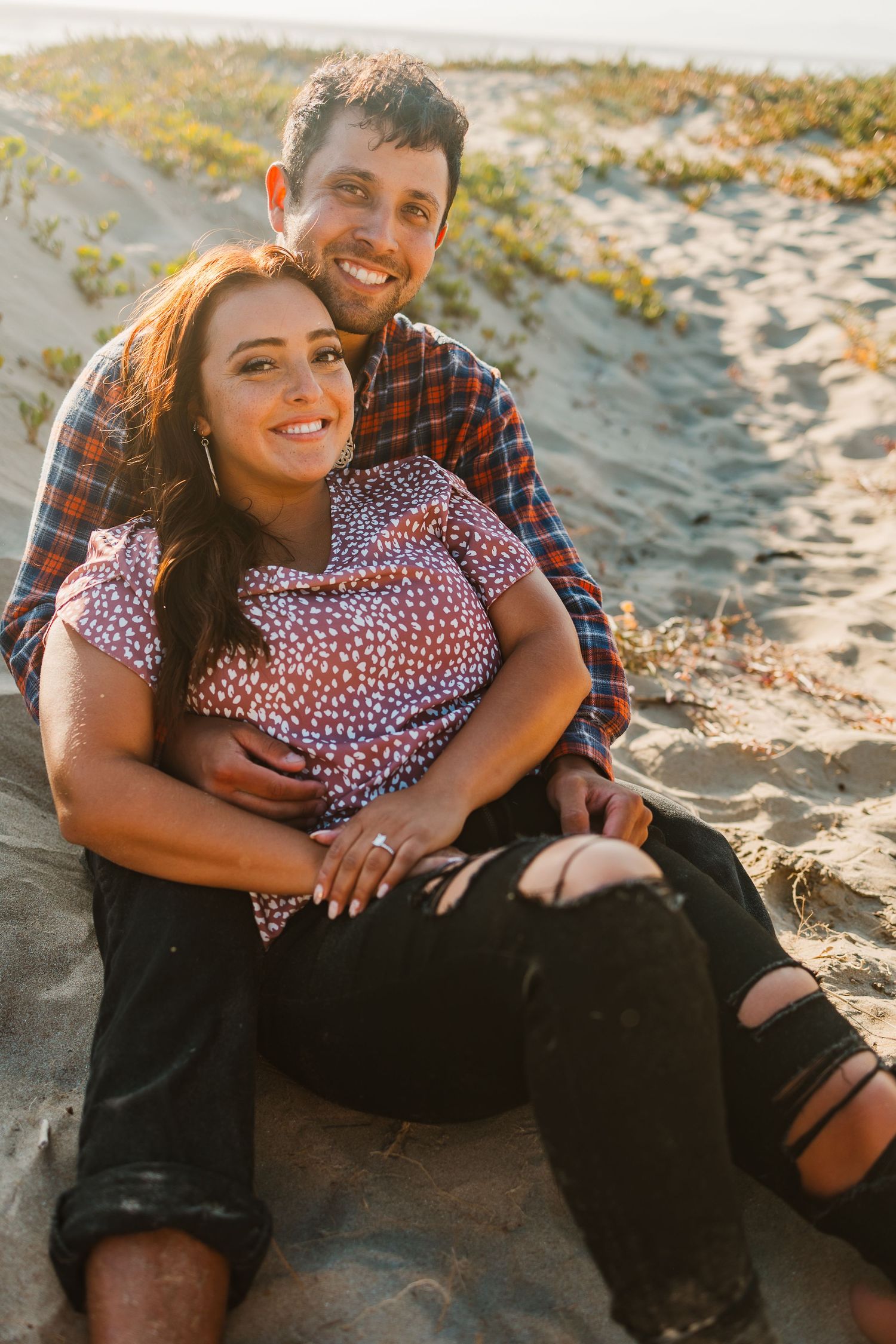 Couple in plaid and polka dots smiling during beach photoshoot.