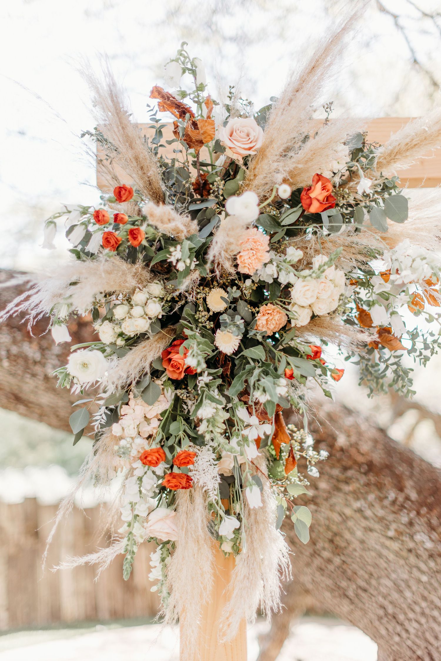 A romantic wedding bouquet with coral and peach roses, pampas grass, and greenery arranged in a boho style.