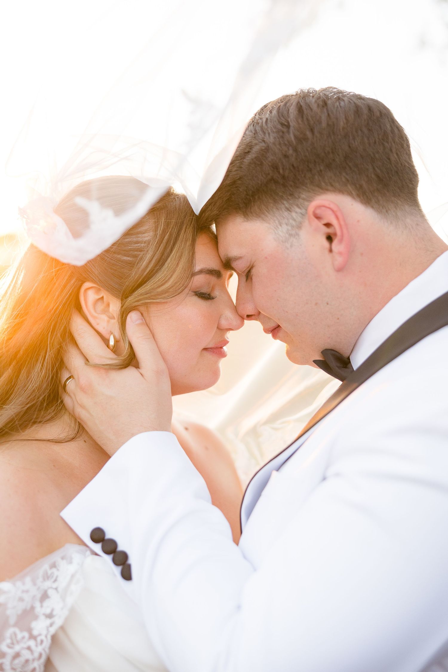 Bride and groom share intimate moment with foreheads touching in golden sunset light.