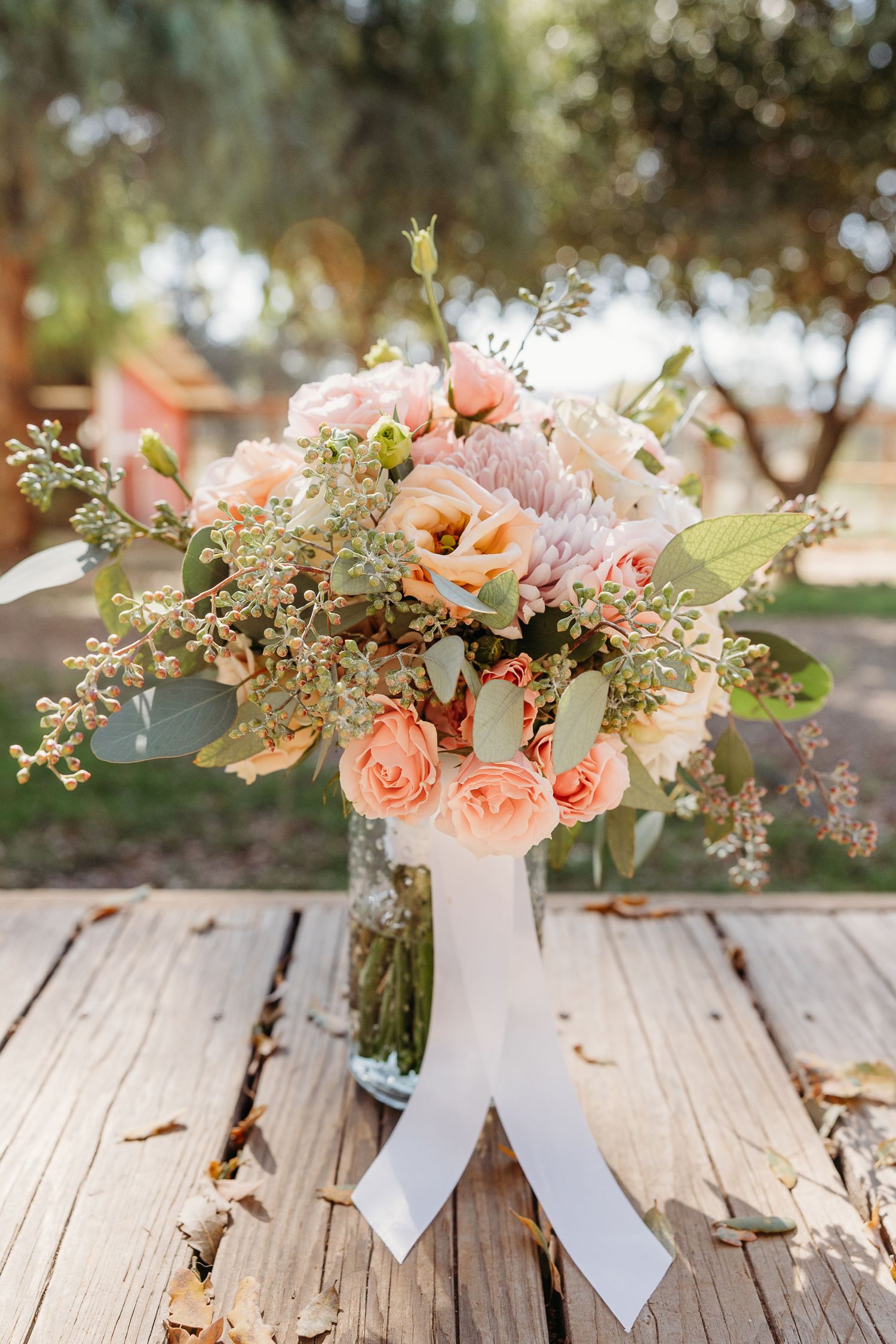 Elegant peach roses and greenery arrangements in white vases displayed on rustic wooden planks.