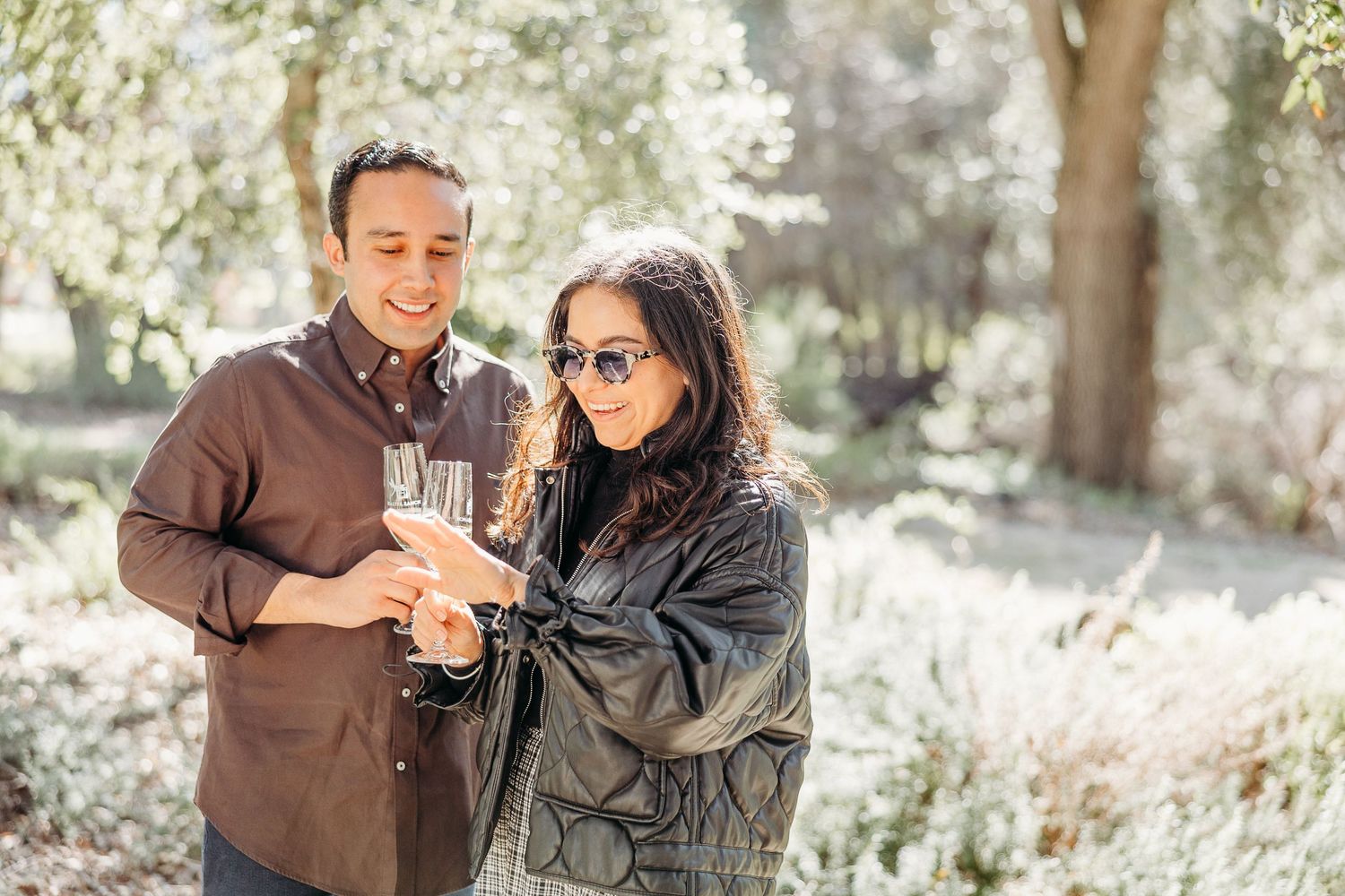 A couple shares a romantic moment together in a sunlit outdoor setting with trees in the background.