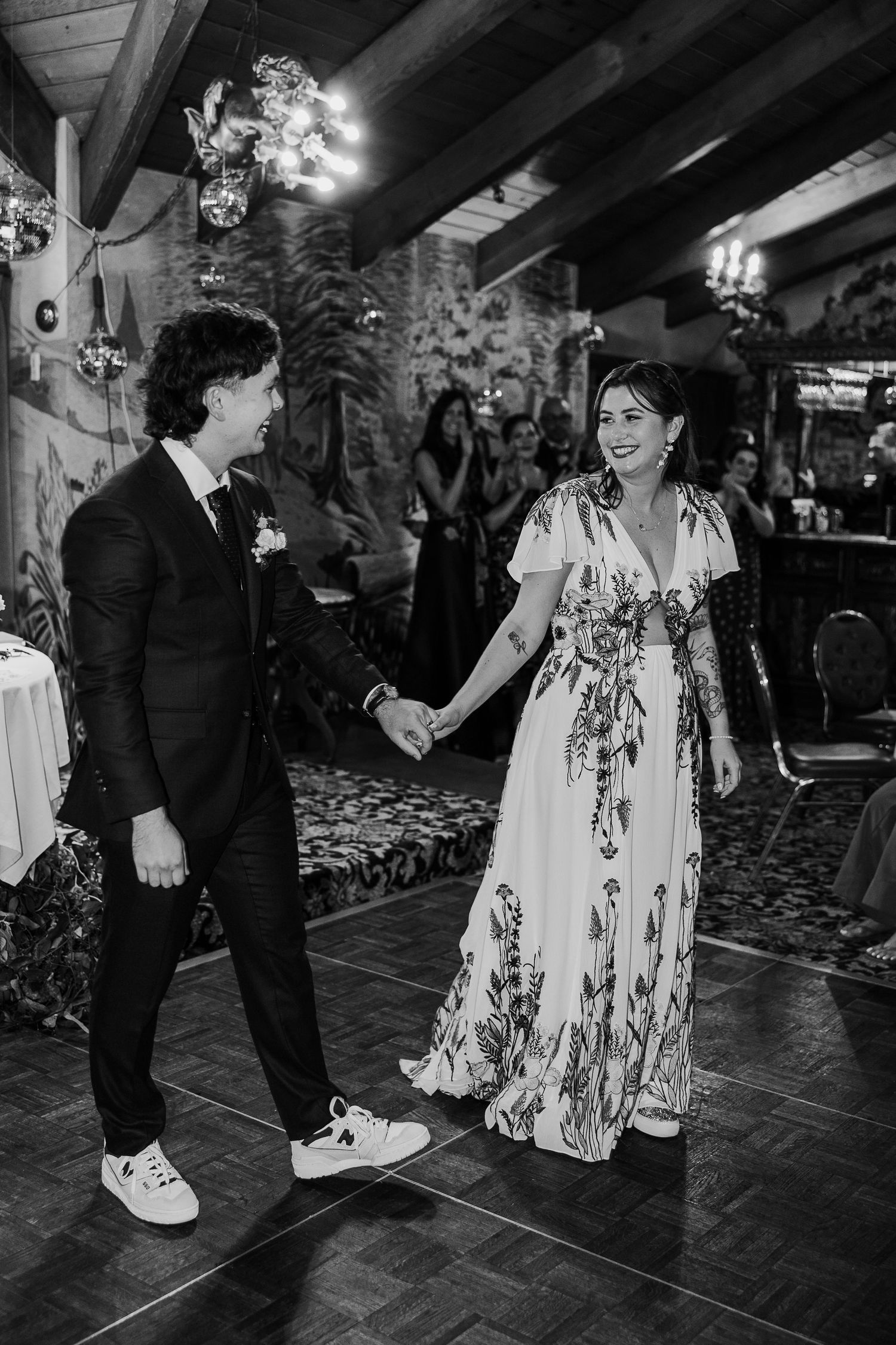 Black and white photo of wedding reception dancing on dark tile floor.