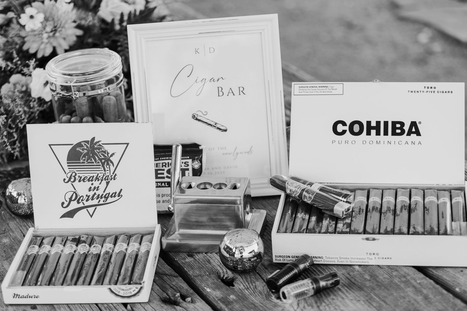 Black and white detail shot of cigar bar setup with various cigars and accessories at wedding reception.