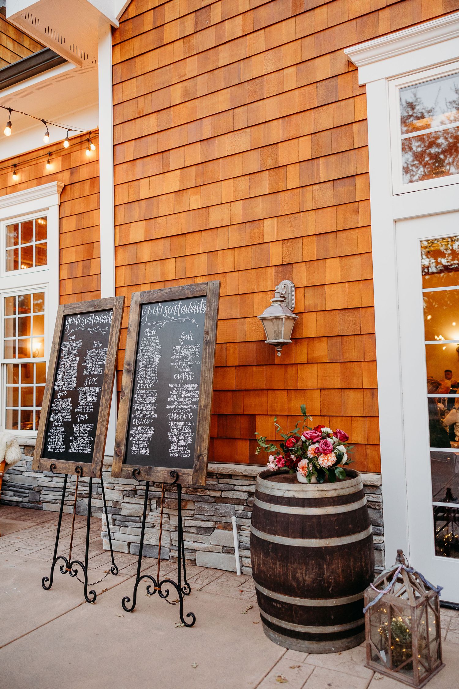 Rustic wedding venue exterior with chalkboard seating charts and wooden barrel decor.